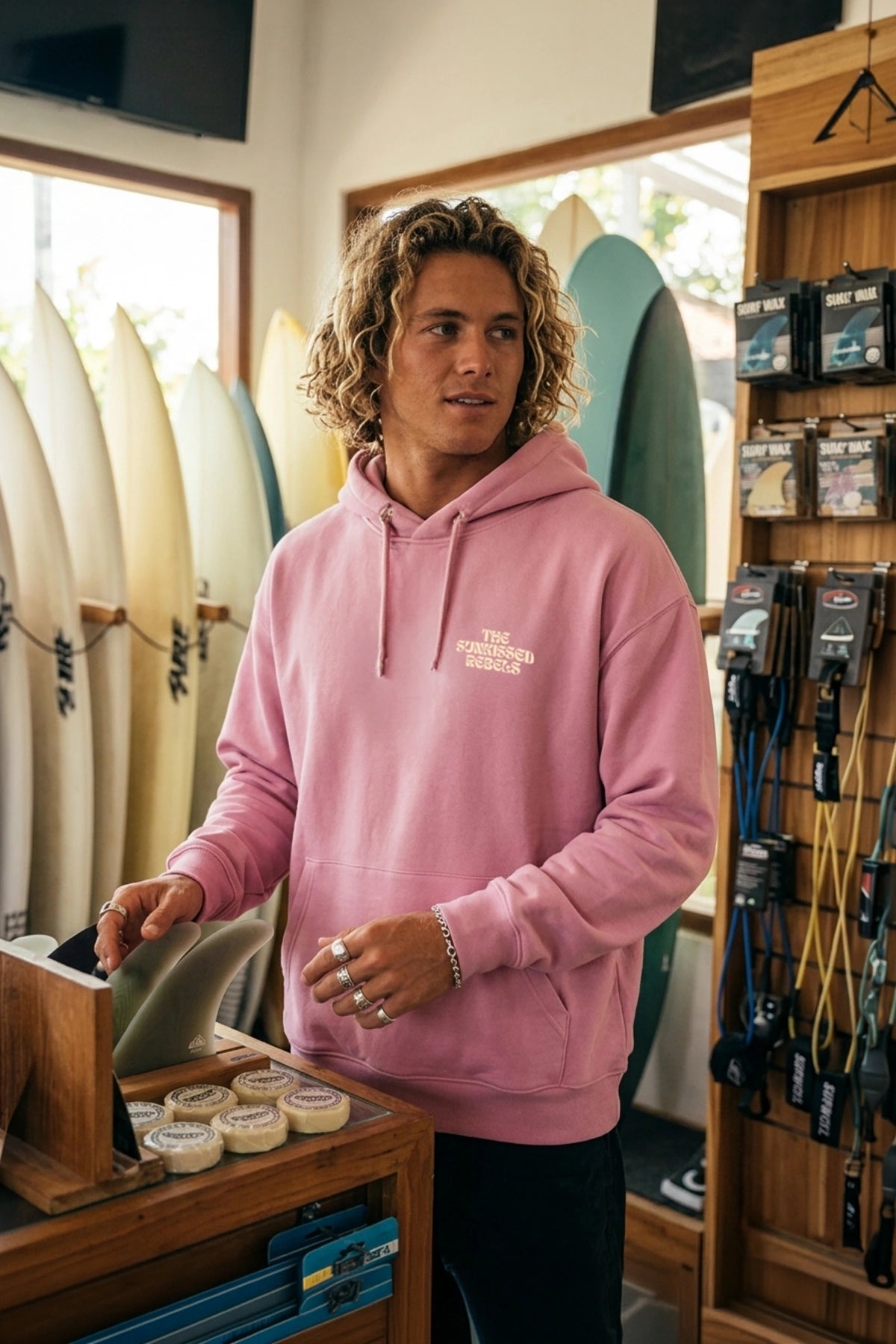 Model trägt pinken A Good Day Hoodie im Surfshop mit lässigem Oversized Fit und Surfboards im Hintergrund