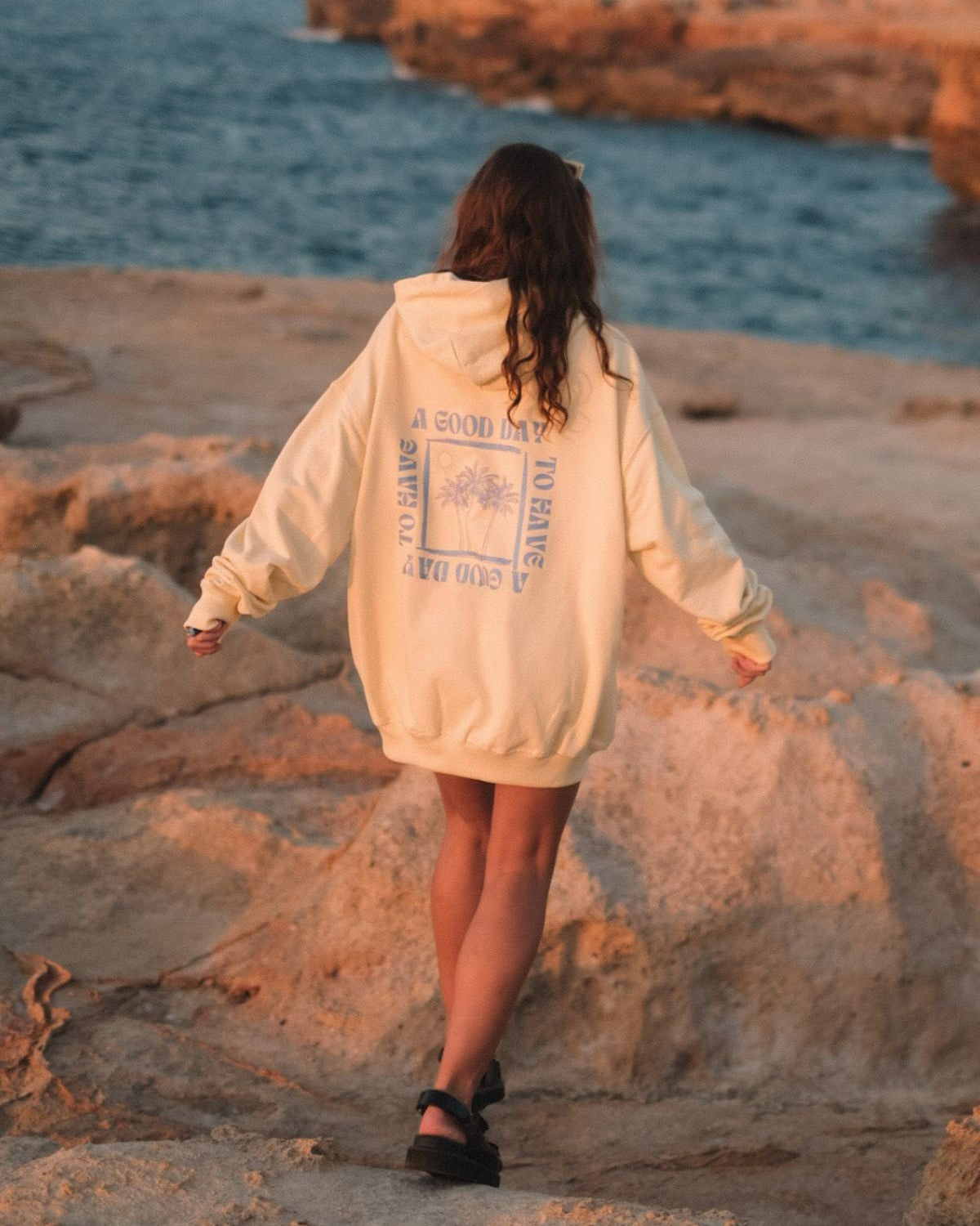 Frau trägt A Good Day Oversized Sweater von The Sunkissed Rebels am Strand im Sonnenuntergang.