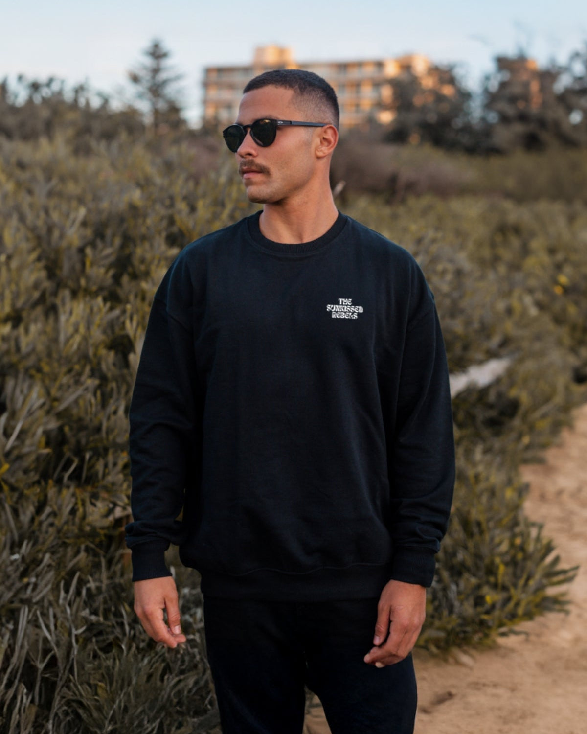 Man trägt schwarzen oversized Sweater von The Sunkissed Rebels am Strand.