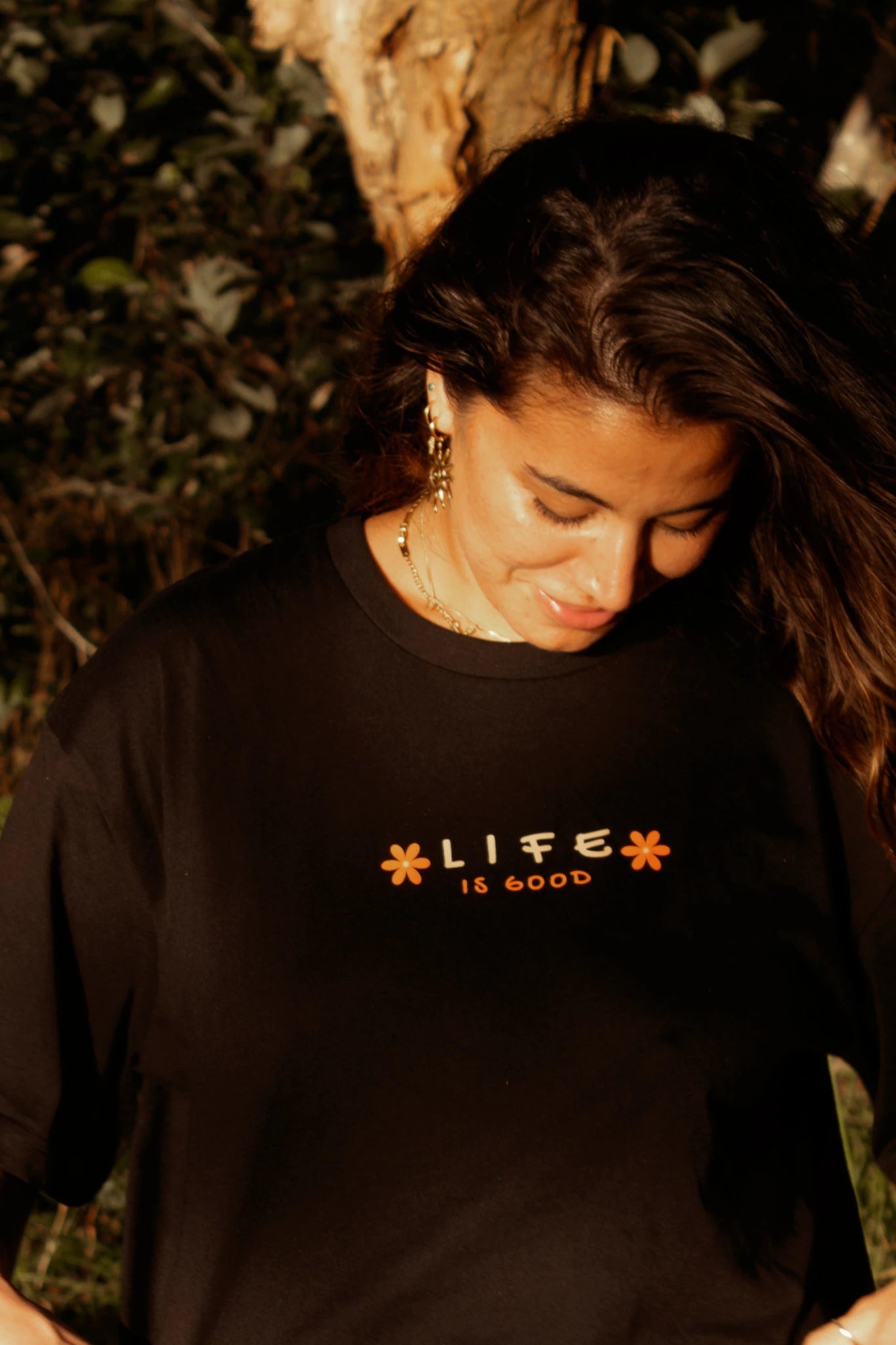 Detailaufnahme eines schwarzen Oversized T-Shirts mit Life is Good Print in Orange bei warmem Sonnenlicht