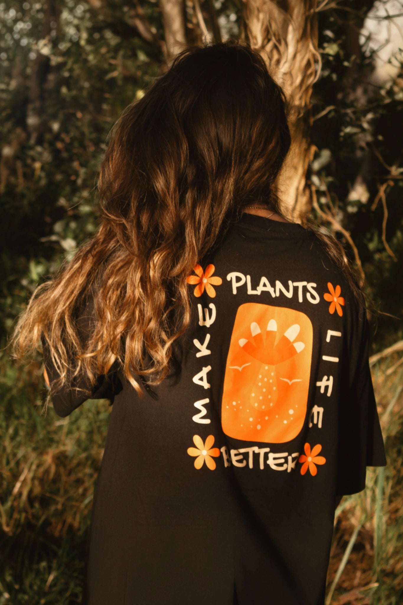 Rückansicht einer Frau mit schwarzem Oversized T-Shirt und großem Plants Make Life Better Print im Natursetting