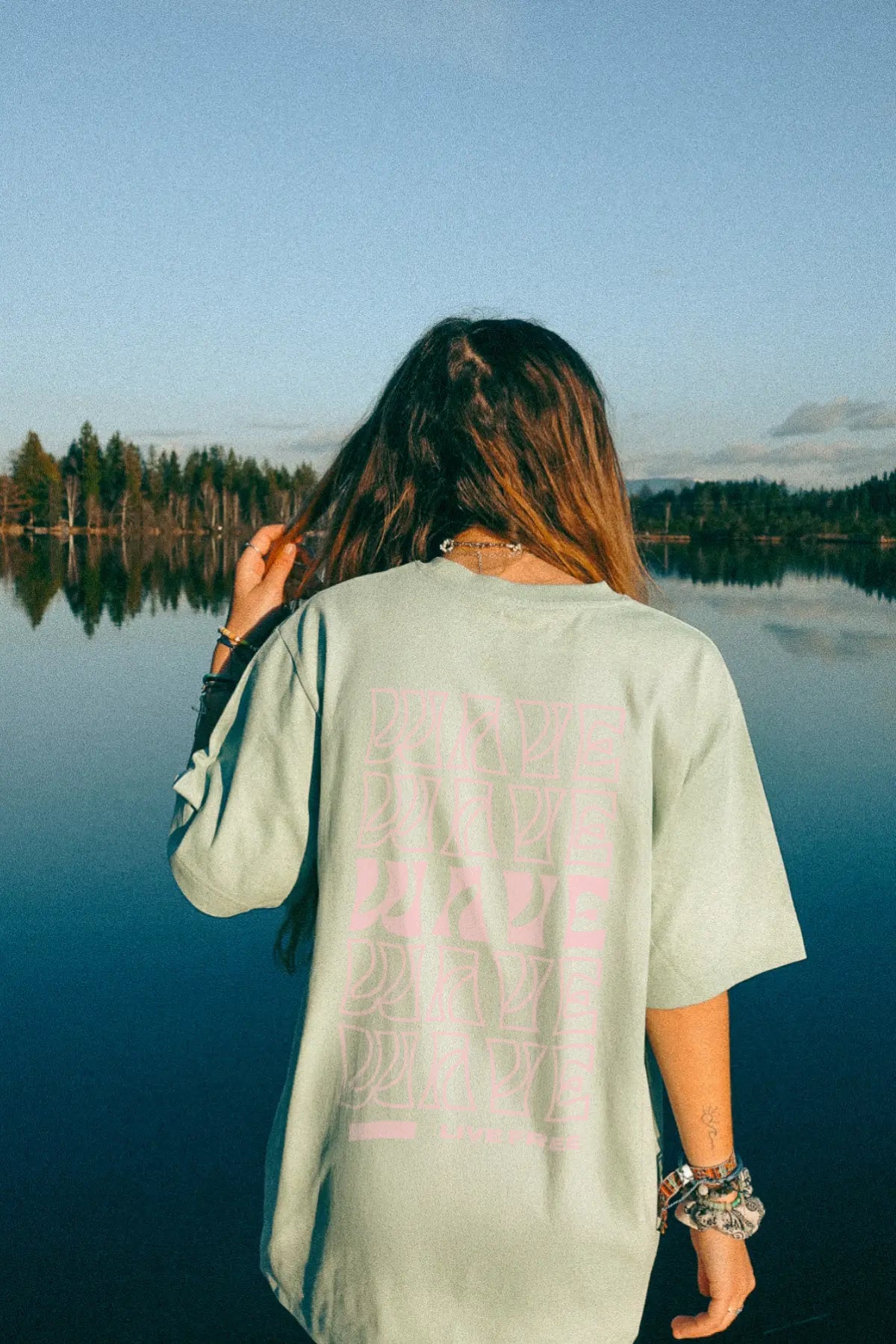 Frau mit mintgrünem Live Free-Shirt in der Morgenstimmung am See mit Blick ins Wasser