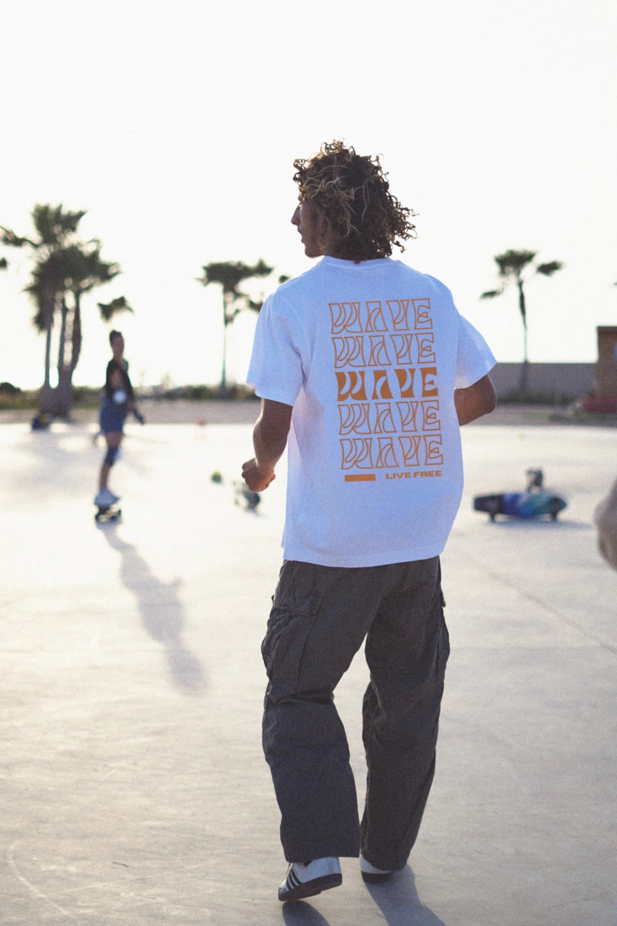 Rückansicht eines Skaters im weißen Oversized T-Shirt mit orangem Live Free Design – The Sunkissed Rebels