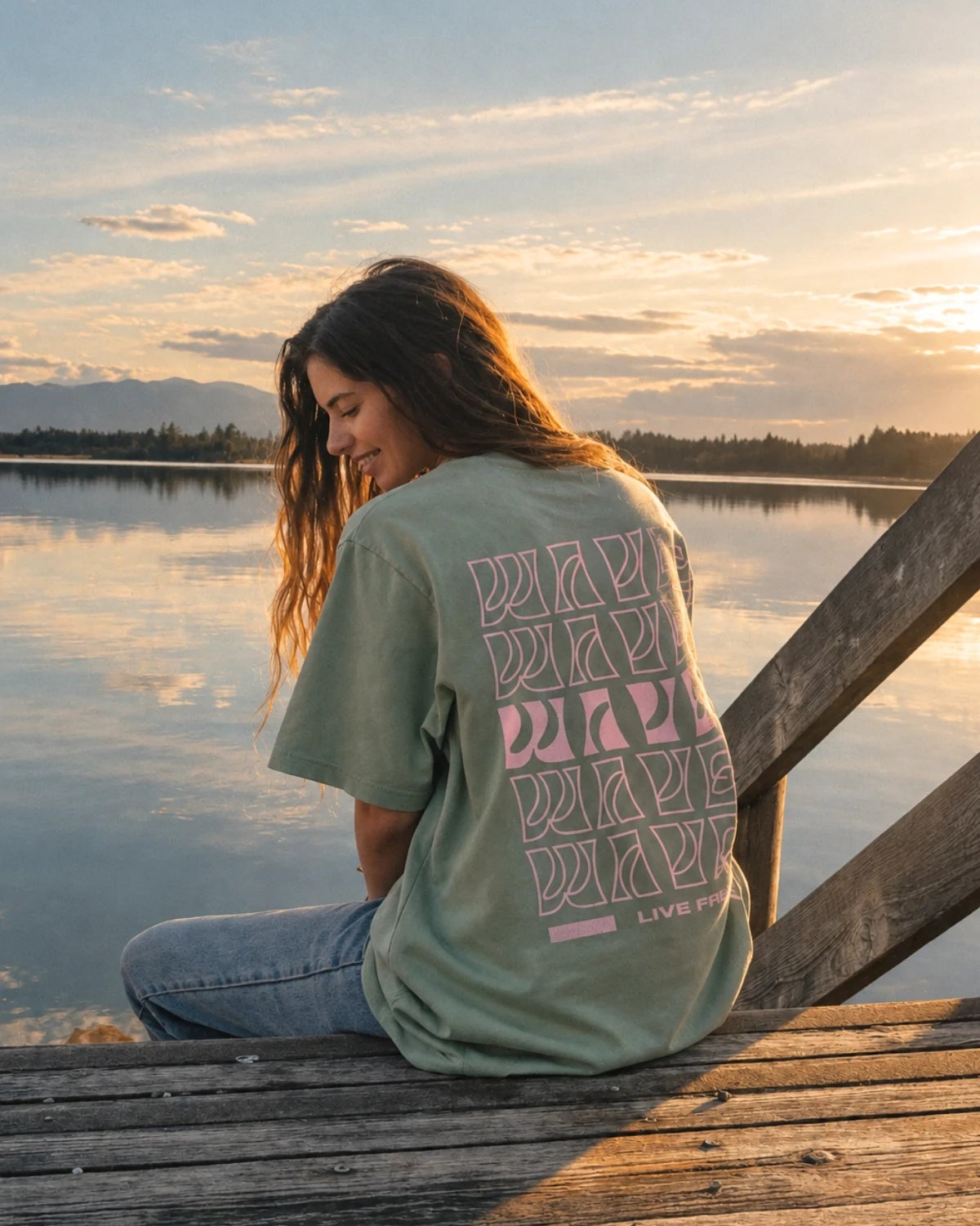 Frau sitzend am Holzsteg im grünen Live Free Oversized T-Shirt Aloe mit rosa Wave Backprint von The Sunkissed Rebels