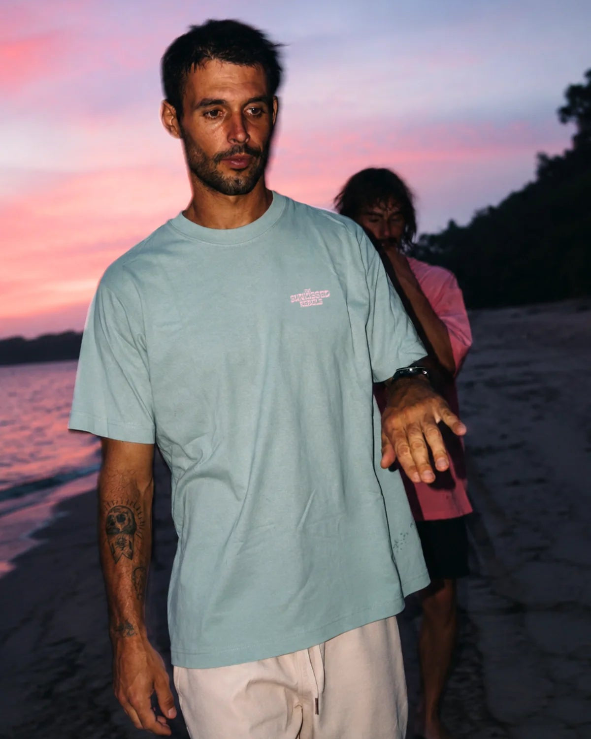 Mann trägt das hellgrüne Live Free Oversized T-Shirt mit Stickerei am Strand während der Dämmerung.