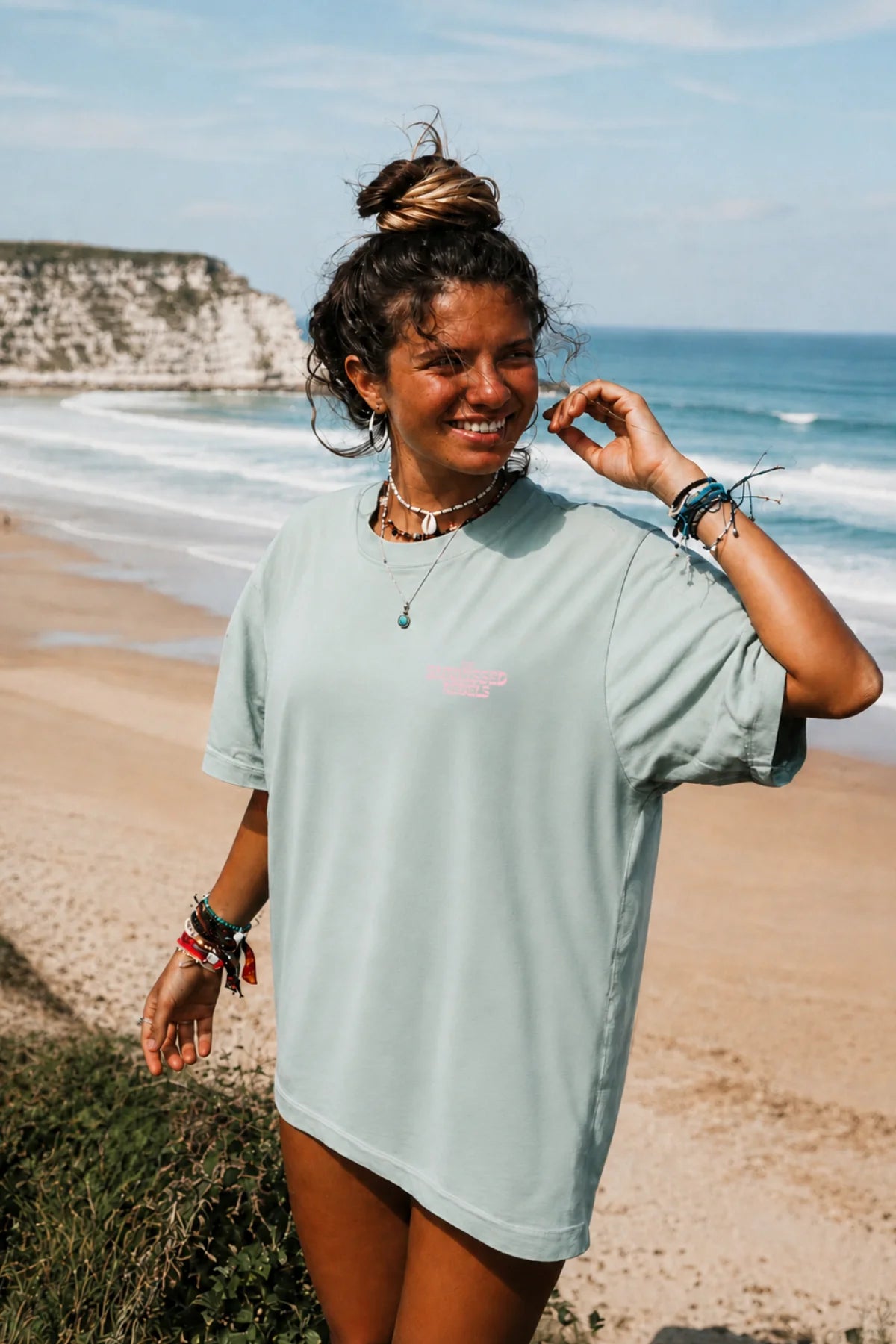 Lächelnde junge Frau am Strand im mintgrünen Live Free Oversized T-Shirt mit kleinem Brustprint.