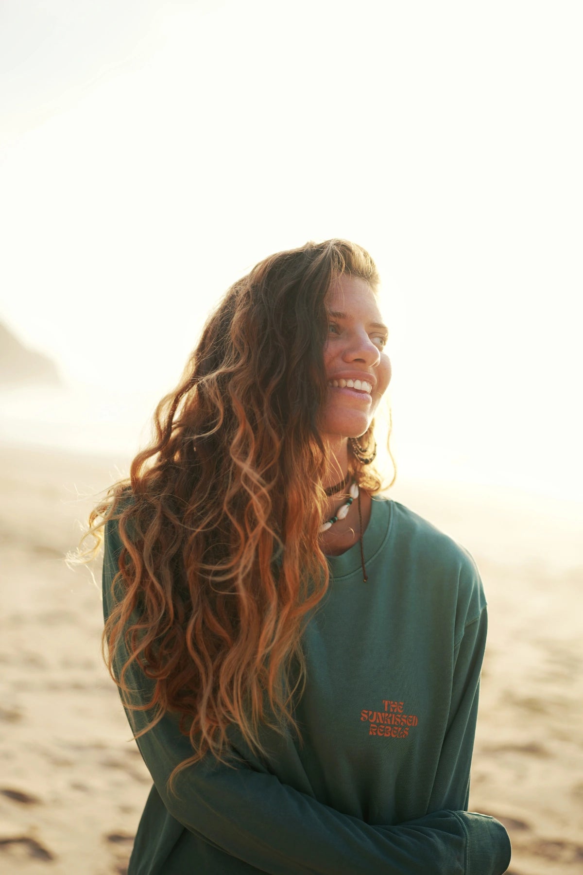 Nahaufnahme – Frau mit Muschelkette lächelt im grünen Sweater am Strand