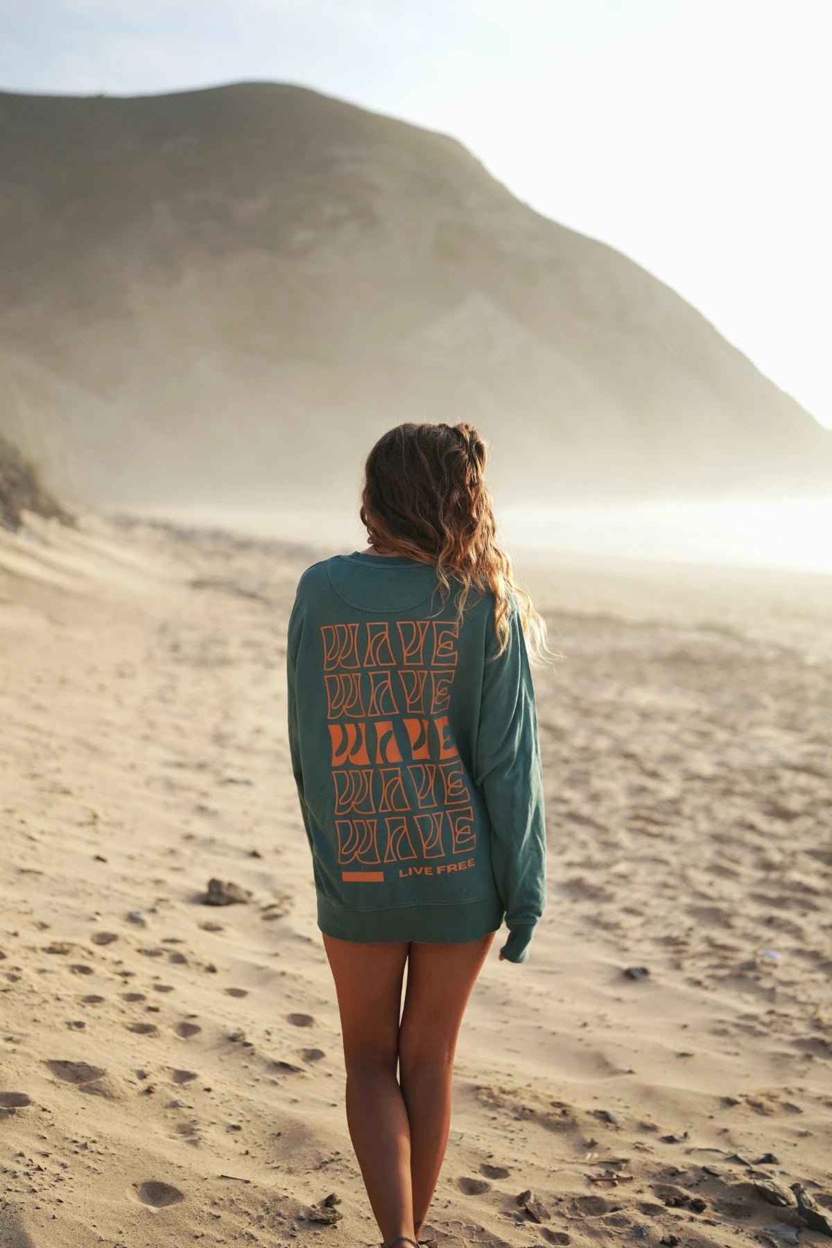 Palm Green Sweater von hinten – Frau blickt Richtung Sonnenuntergang