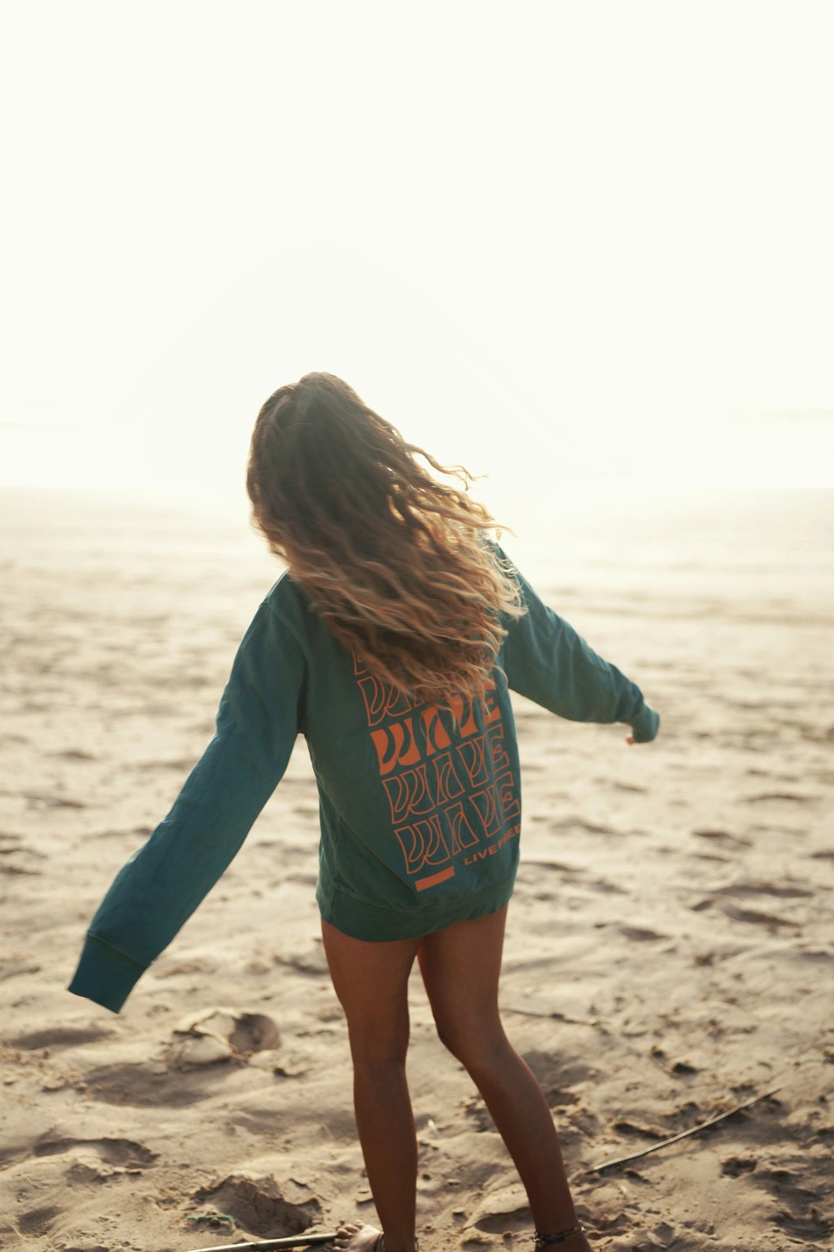 Frau tanzt frei im Palm Green Sweater mit Rückenprint bei Sonnenuntergang