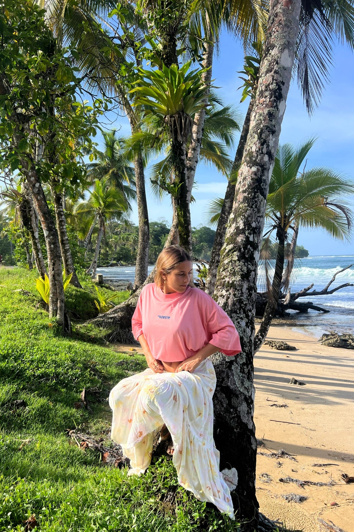 Lifestyle-Foto des Pink Joy No Bullshit Whale Boxy Oversized T-Shirts vor tropischer Strandkulisse mit Palmen und Ozean.