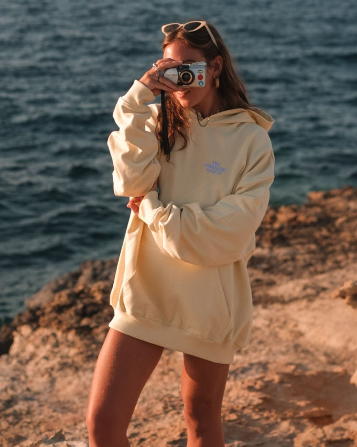 Frau trägt A Good Day Hoodie in butter am Strand un macht ein Foto.