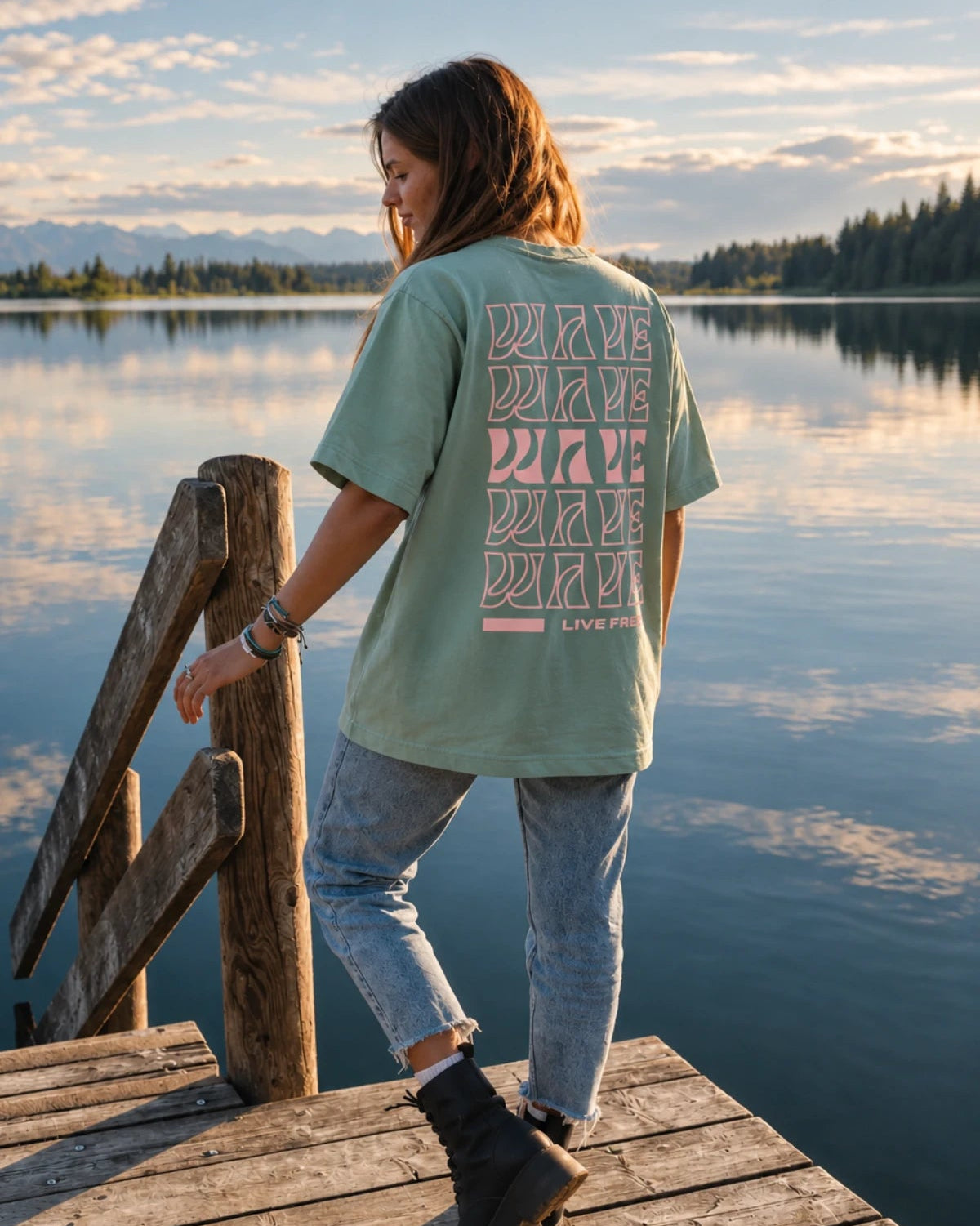 Rückansicht des Live Free Oversized Shirts in Aloe kombiniert mit Jeans und Boots am See – The Sunkissed Rebels