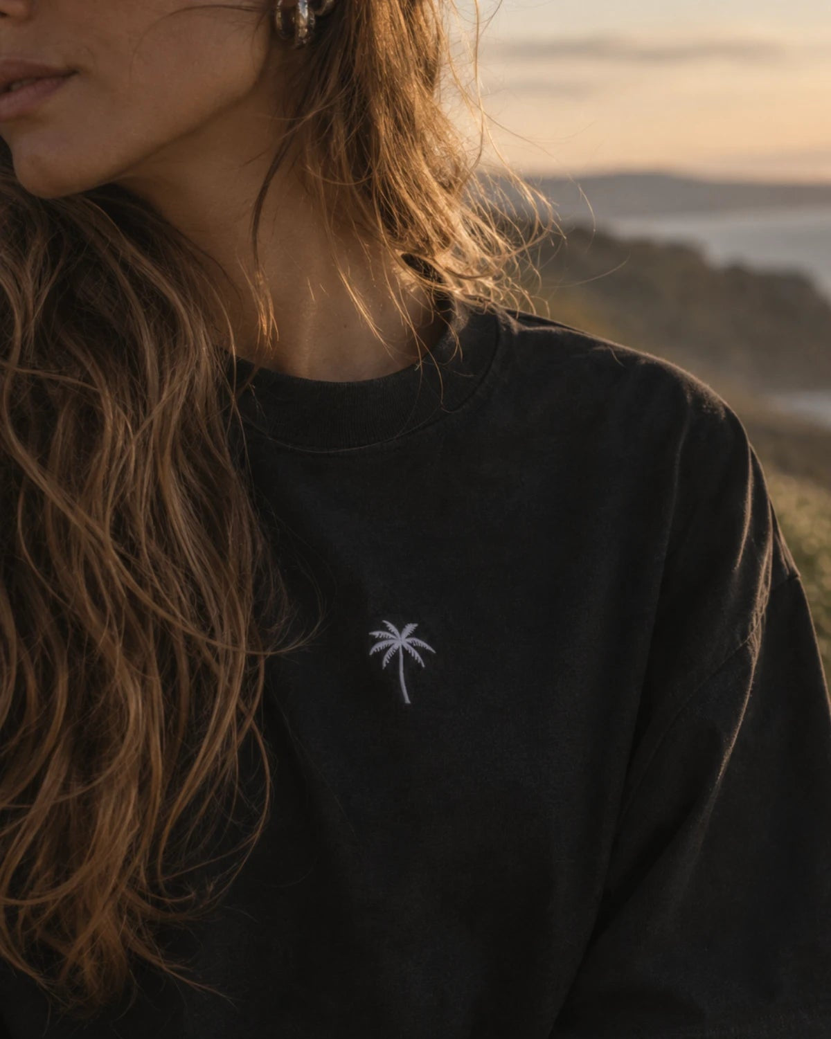 Nahaufnahme der weißen Palmen-Stickerei auf der Brust des schwarzen Palm Tree Boxy Oversized T-Shirts von The Sunkissed Rebels.