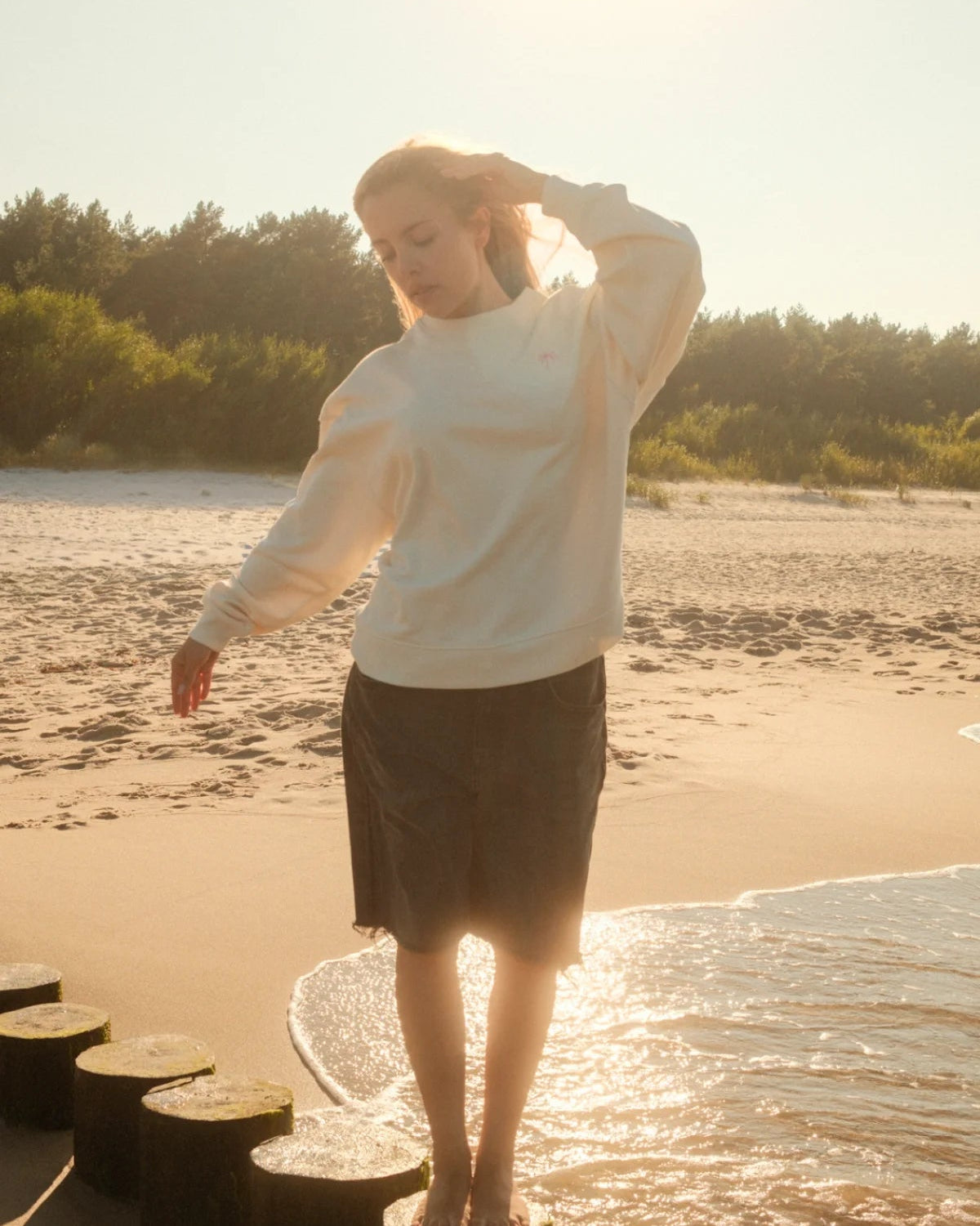 Entspannter Coastal Style mit beigem Palm Tree Oversized Sweater von The Sunkissed Rebels und Jeans-Shorts am Meer.