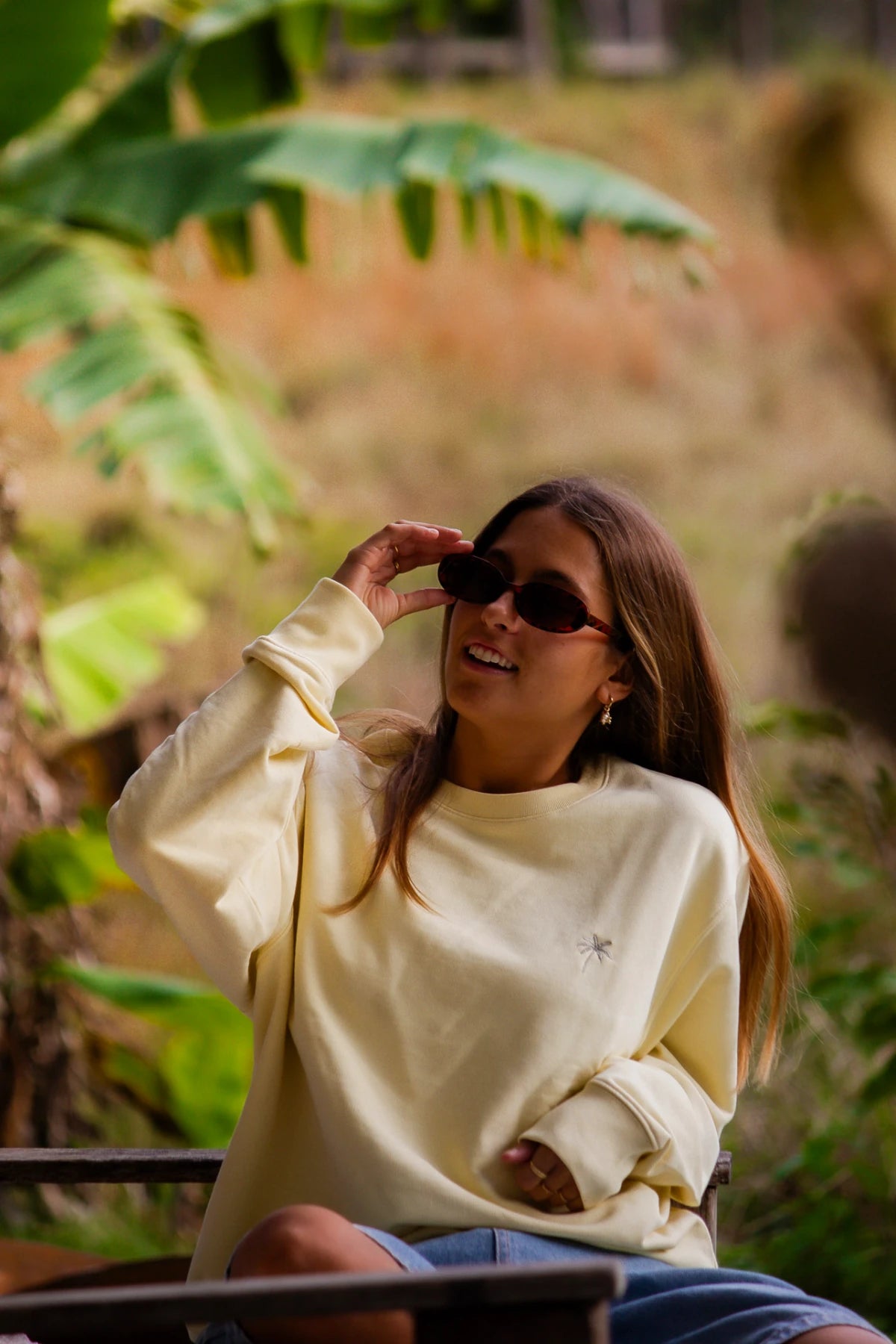 Frau mit Sonnenbrille lacht entspannt im Palm Tree Sweater in Butter bei natürlichem Licht