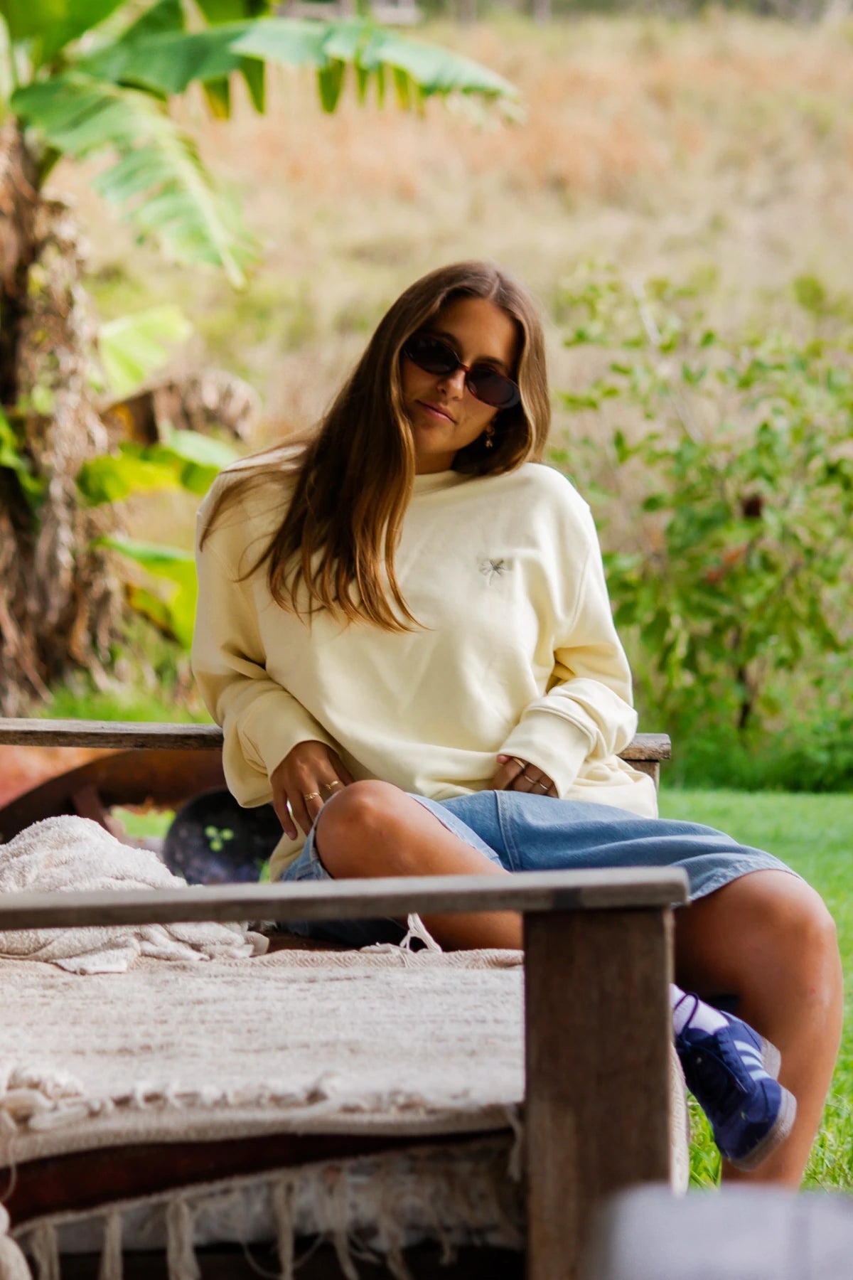 Relaxte Pose auf Outdoor-Couch mit dem butterfarbenen Palm Tree Sweater und Denim Shorts