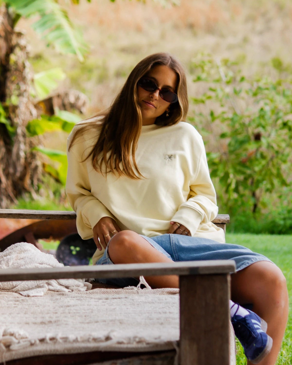 Relaxte Pose auf Outdoor-Couch mit dem butterfarbenen Palm Tree Sweater und Denim Shorts