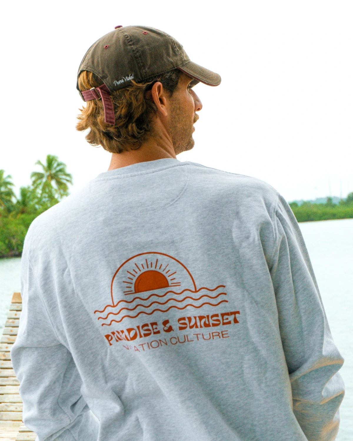Schräg aufgenommene Rückansicht des Paradise & Sunset Sweaters in Cool Grey mit großem Paradise & Sunset Print am Wasser.