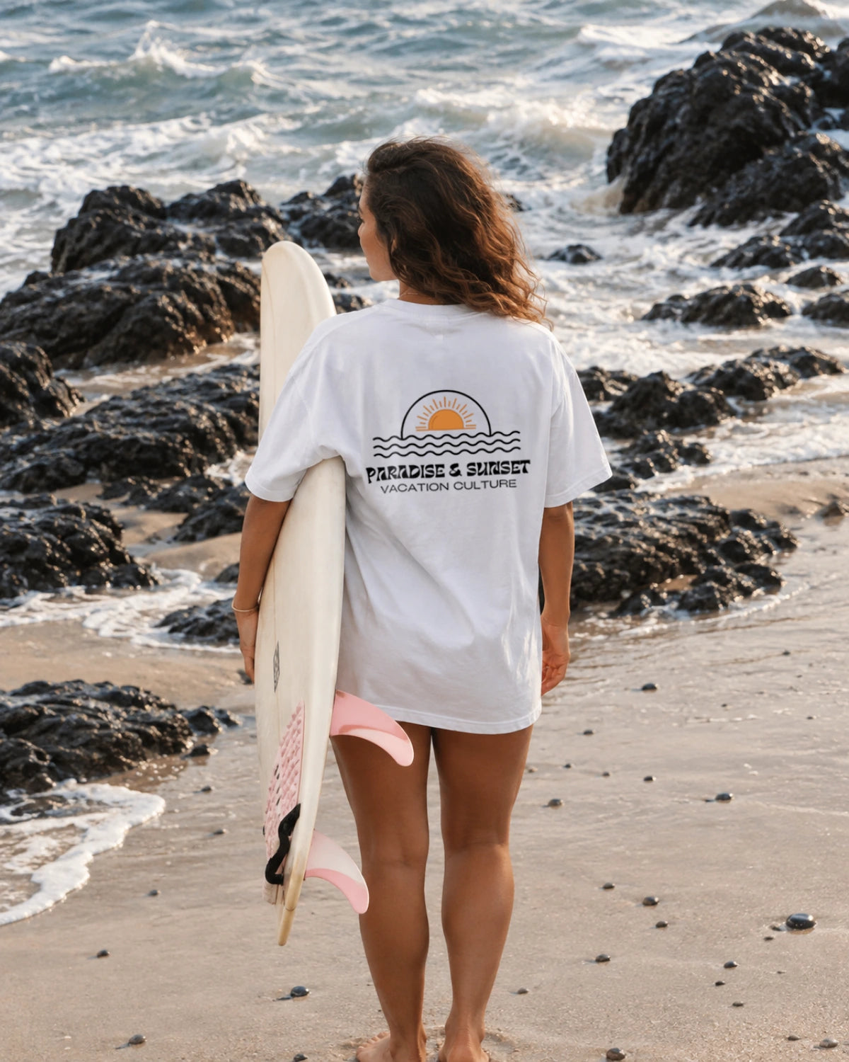 Frau trägt das Paradise & Sunsets Oversized T-Shirt in White mit großem Sun & Waves Rückenprint am Strand