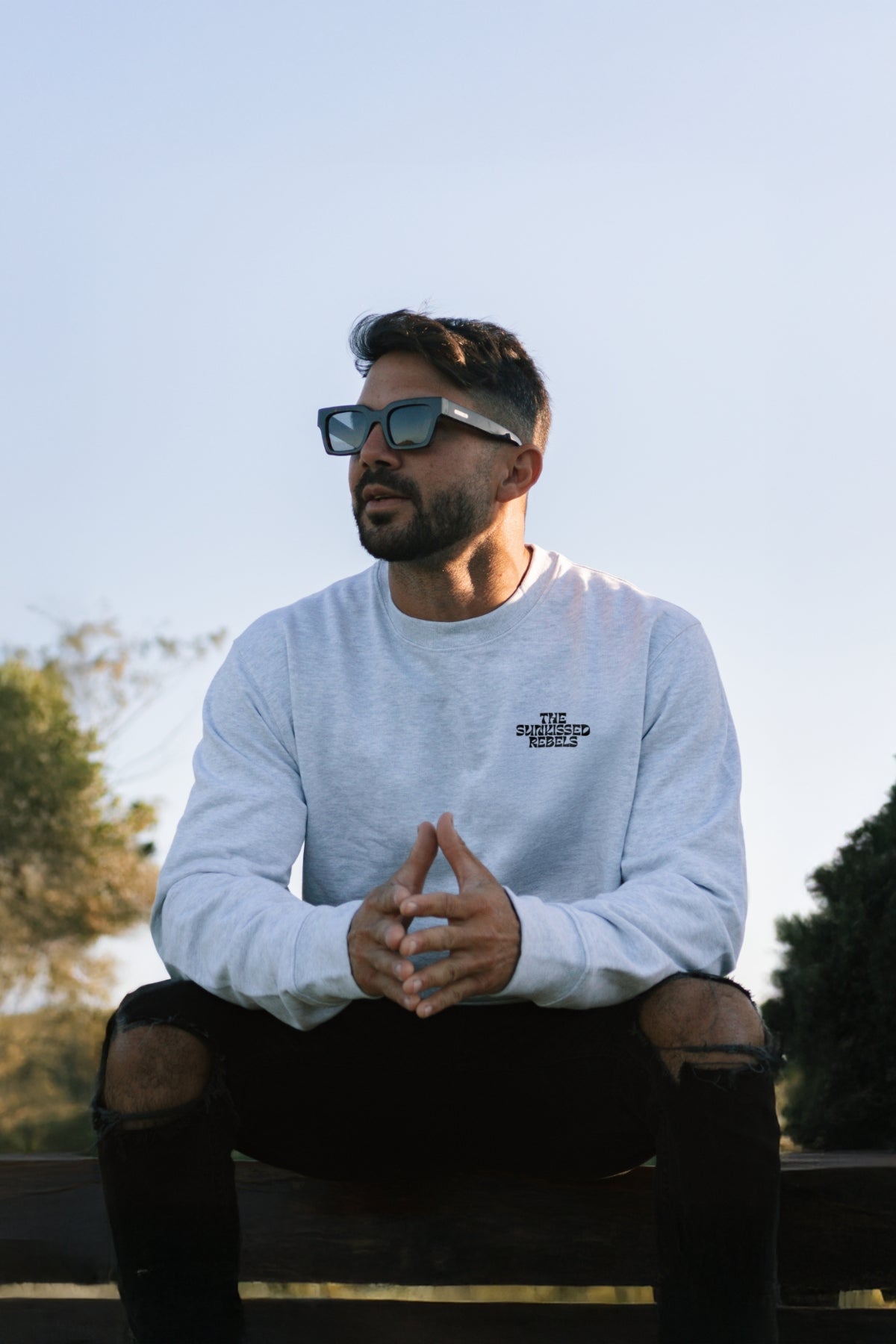 Mann sitzt auf Bank und guckt auf Meer. Trägt grauen Sweater