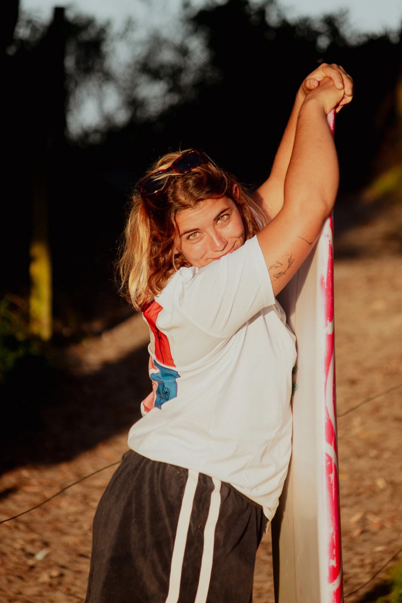 Nahaufnahme einer Frau mit Surfboard im weißen Rebel Elements T-Shirt bei goldenem Licht