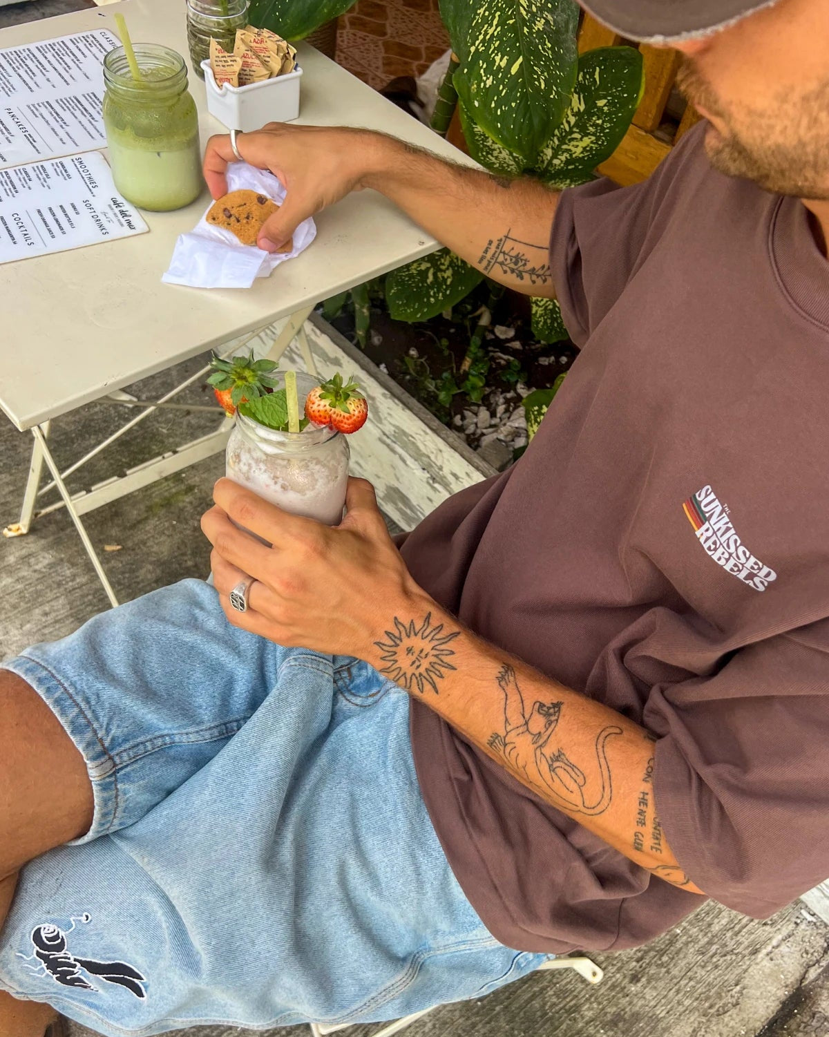 Mann trägt das Retro Vibes Heavy T-Shirt in Mocha mit kleinem Brustlogo in einem gemütlichen Café während des Frühstücks.