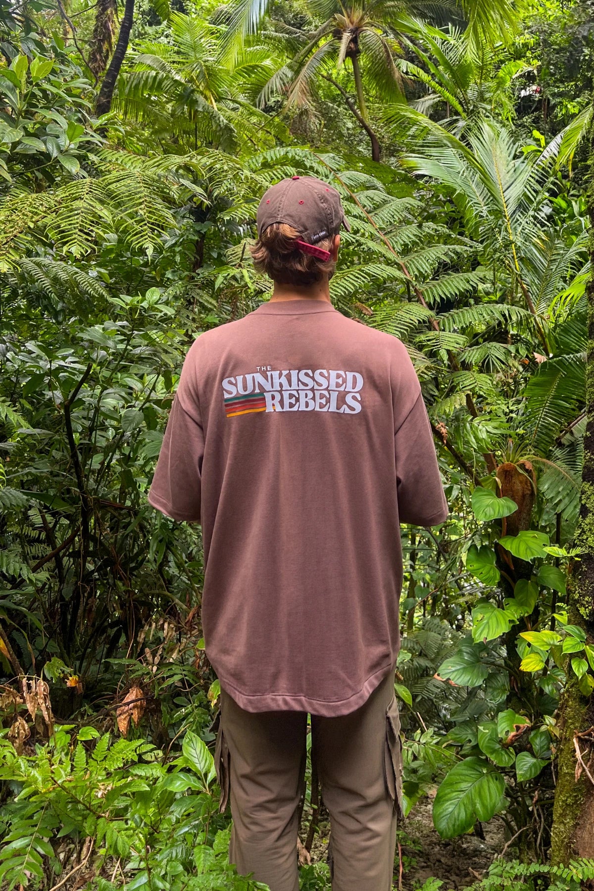 Rückenansicht des Retro Vibes Heavy T-Shirts in Mocha mit großem Retro-Print vor einer tropischen Dschungelkulisse.