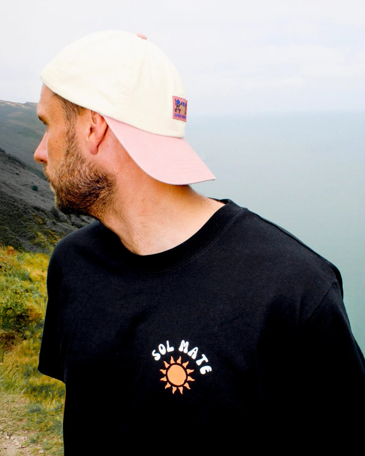Nahaufnahme des Sol Mate Oversized T-Shirts in Schwarz mit Sonnen-Print auf der Brust, getragen in einer Küstenlandschaft.