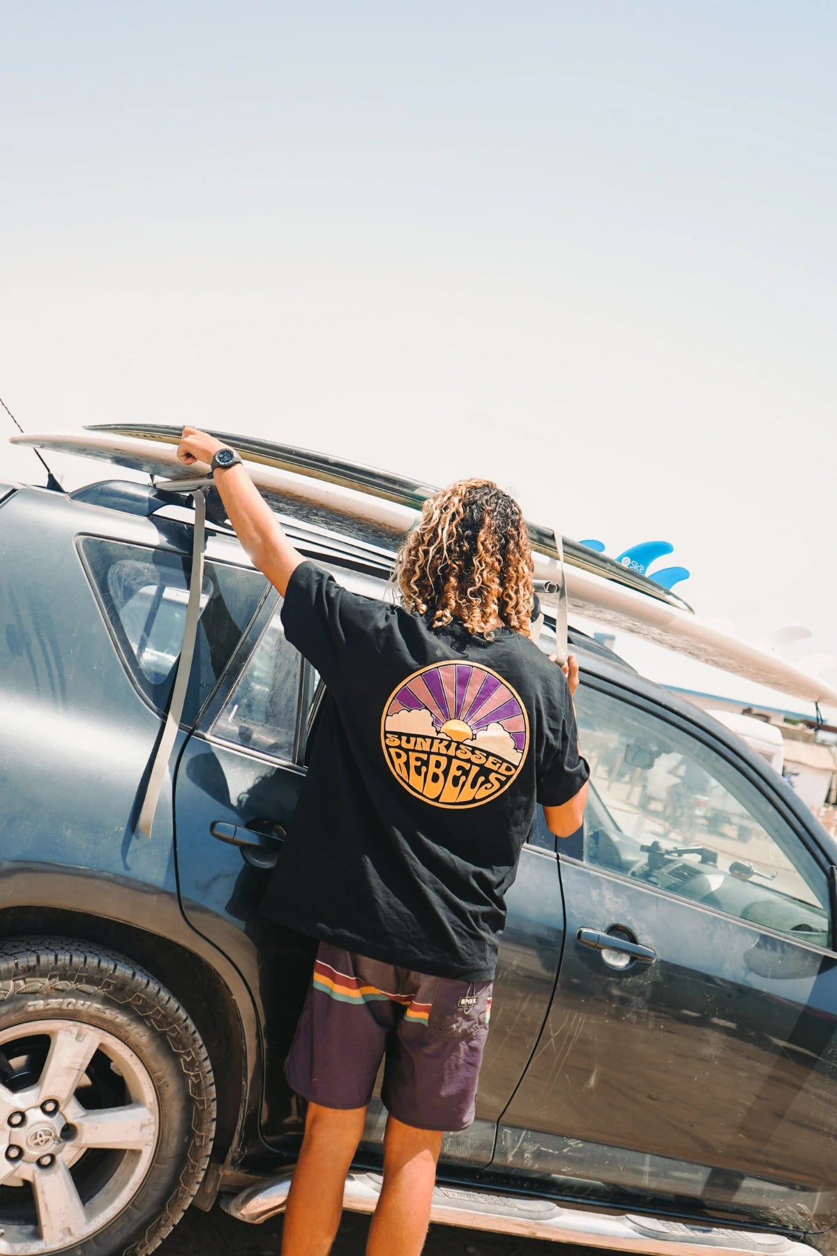Surfer befestigt Surfbrett auf Autodach – Sunkissed Rebels Lifestyle
