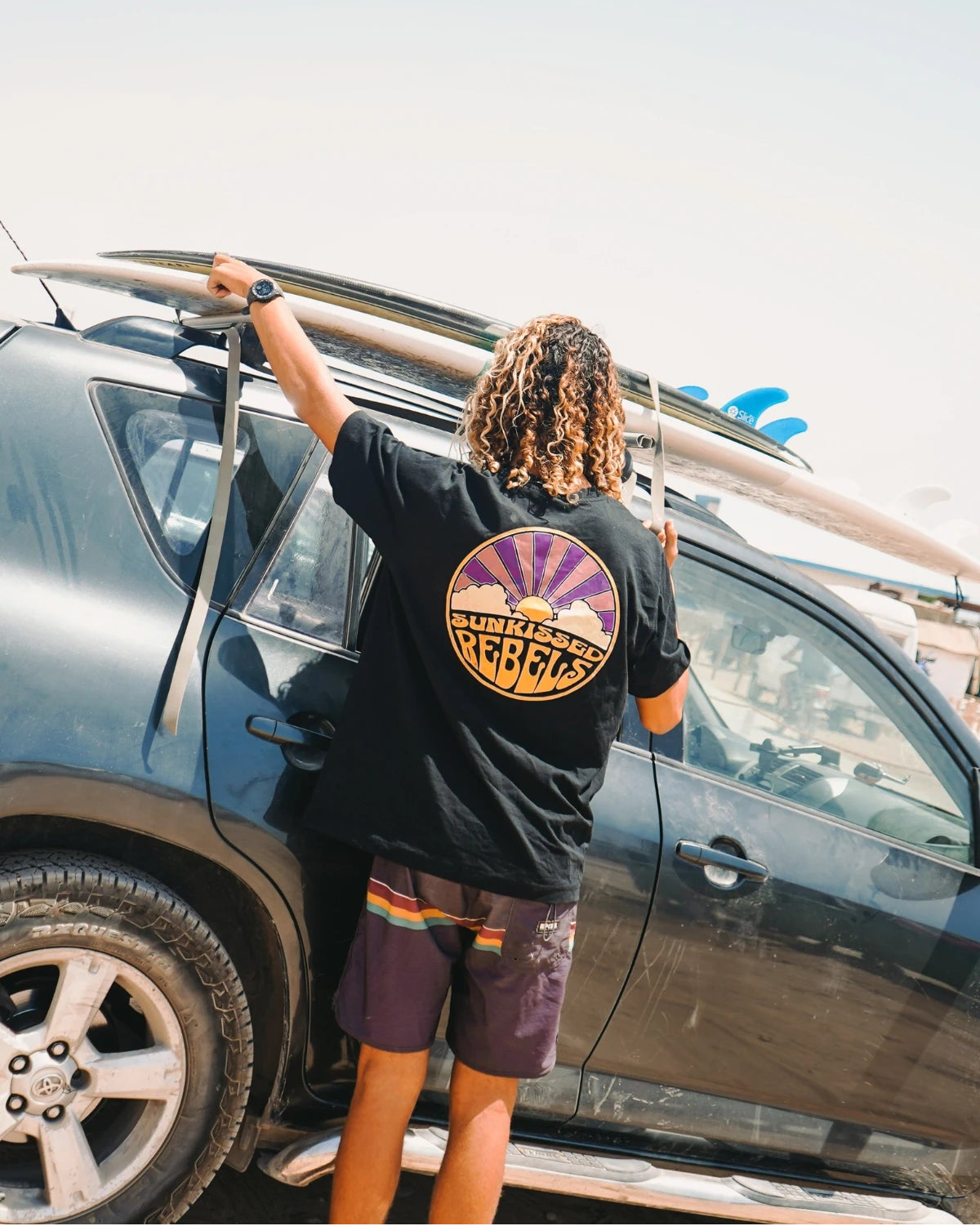 Surfer befestigt Surfbrett auf Autodach – Sunkissed Rebels Lifestyle