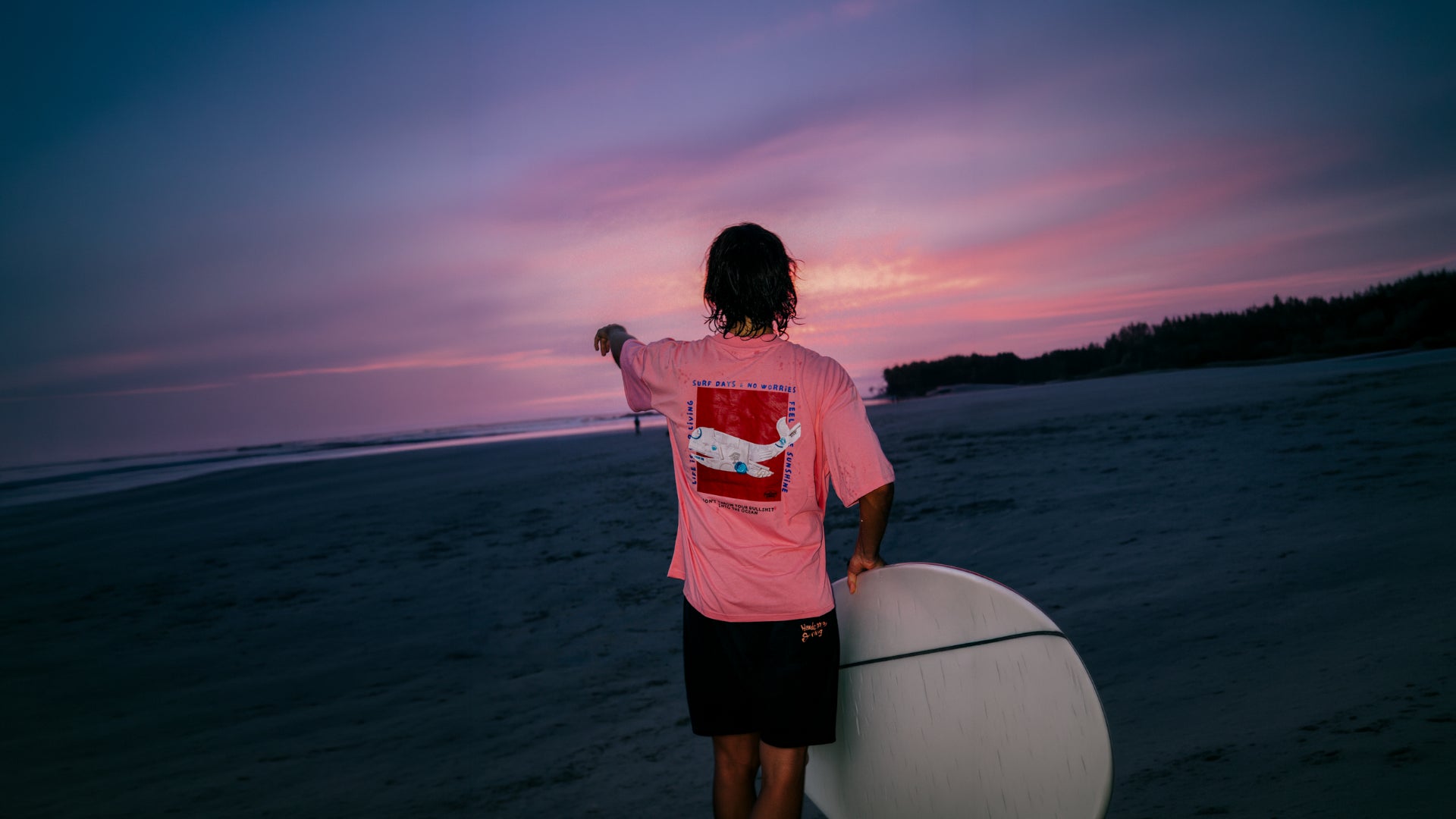 Rückansicht des pinken Surf Days Oversized T-Shirts von The Sunkissed Rebels mit großem Rückenprint und Surfboard am Strand.
