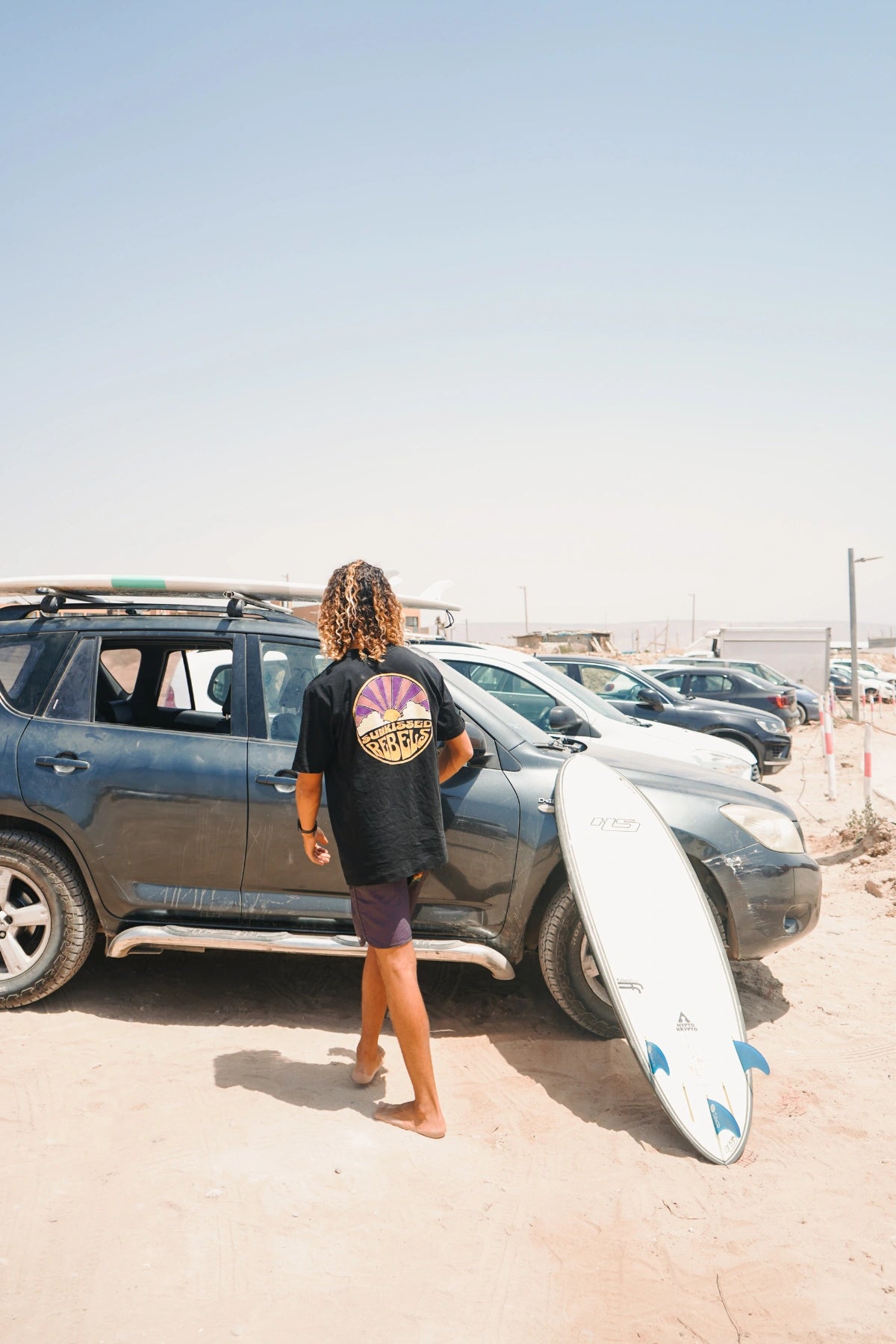Barfuß am Strand – Surfer mit Board und Sunkissed Rebels Shirt