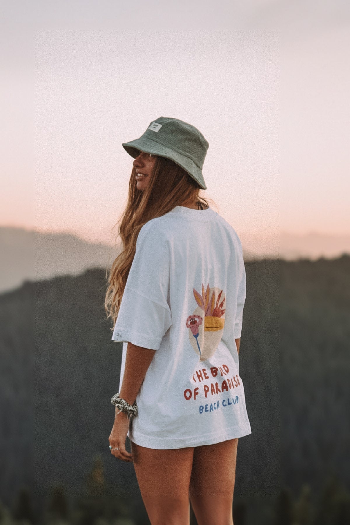 Frau steht auf Berg und trägt Oversized T-Shirt von The Sunkissed Rebels mit Bird of Paradise Print
