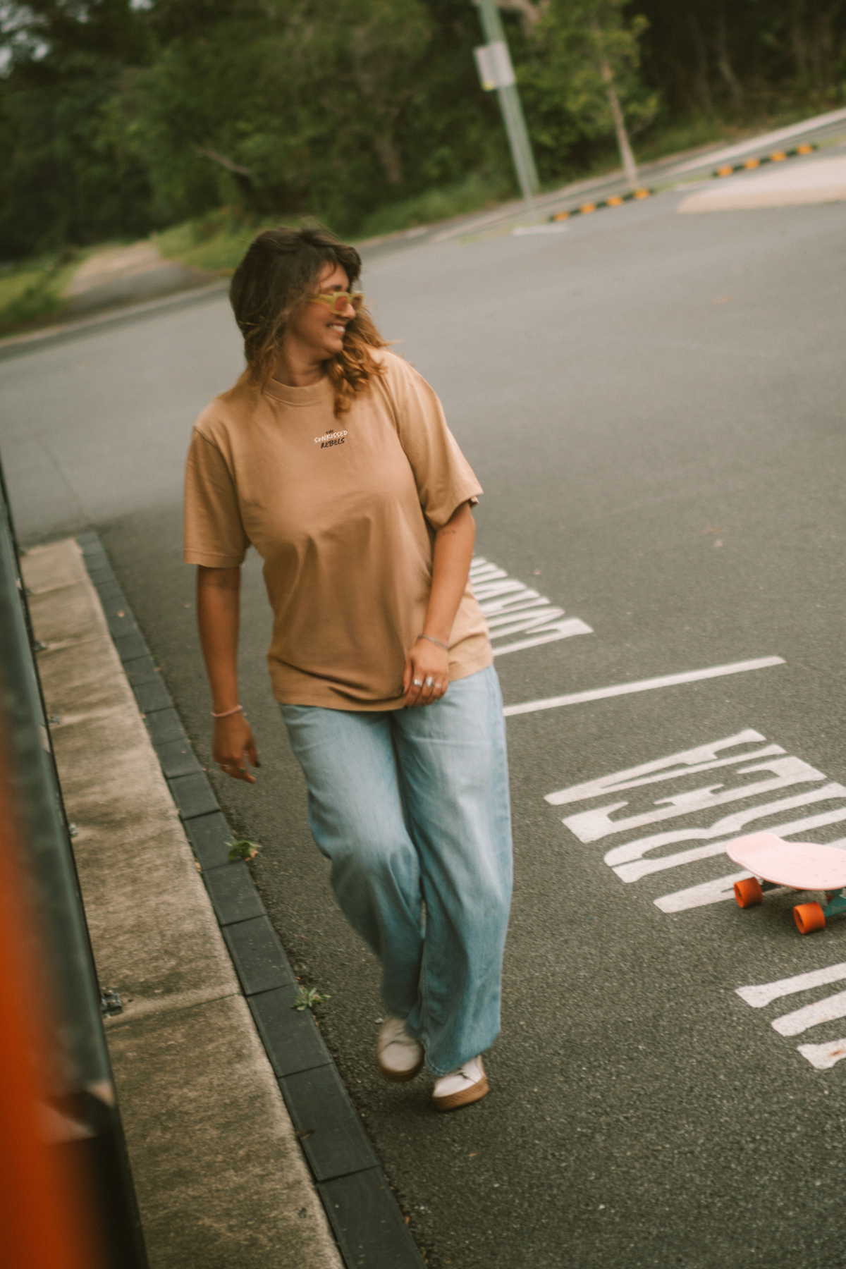 Frau trägt beim Skateboarding ein T-Shirt mit The Sunkissed Rebels Aufschrift.