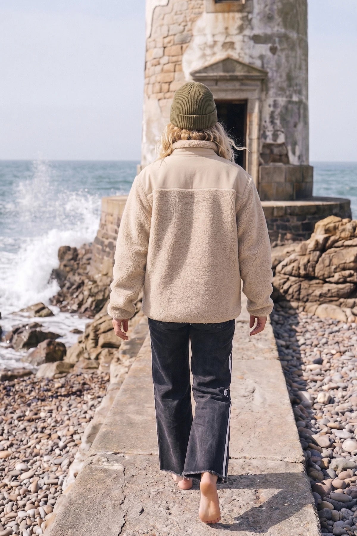 Beige Teddy Fleecejacke für Damen in Rückenansicht an einer felsigen Küste mit Meereswellen im Hintergrund.