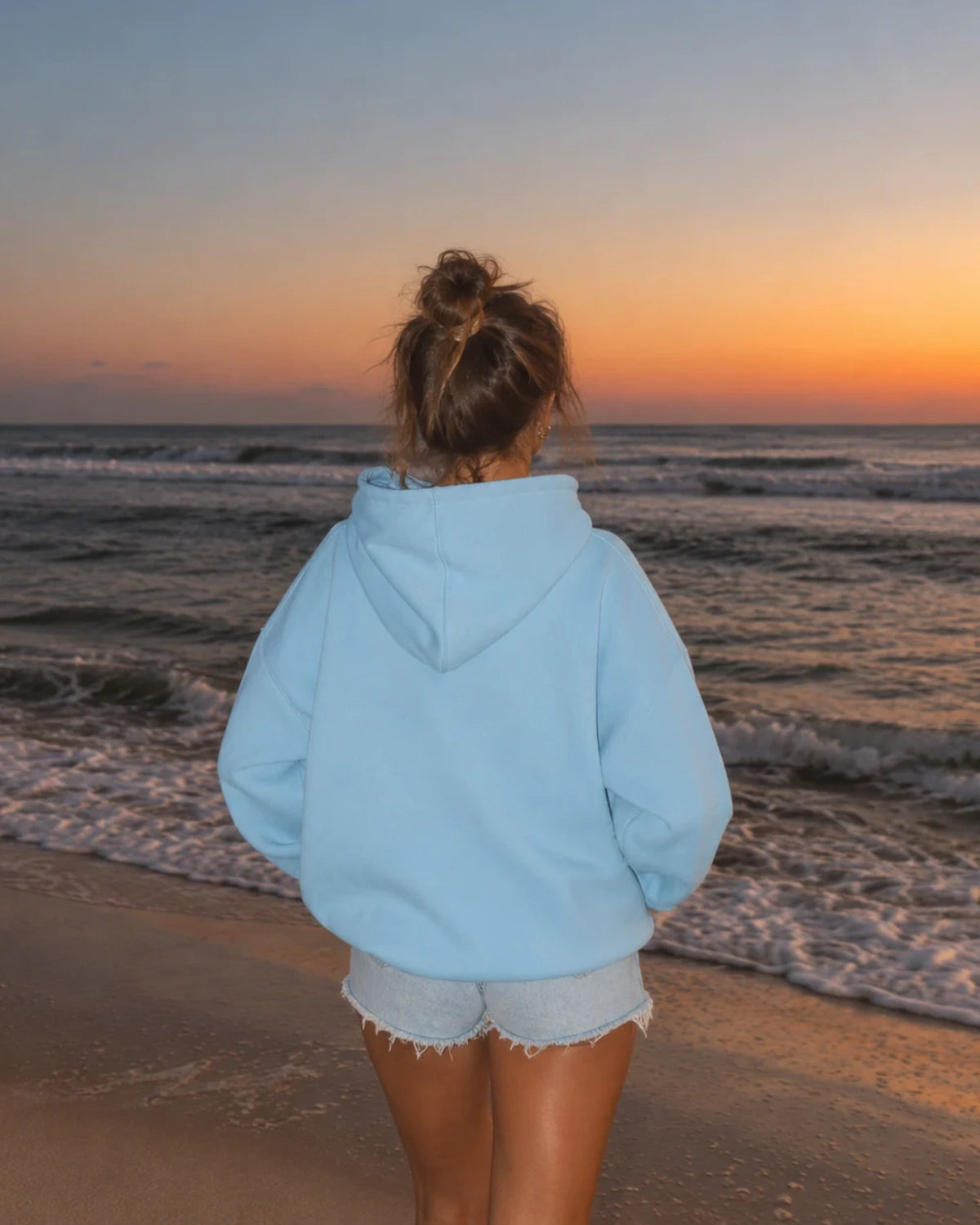 Rückansicht des oversized The Horizon Hoodie – Blue Soul am Strand mit Meer und Sonnenuntergang im Hintergrund.