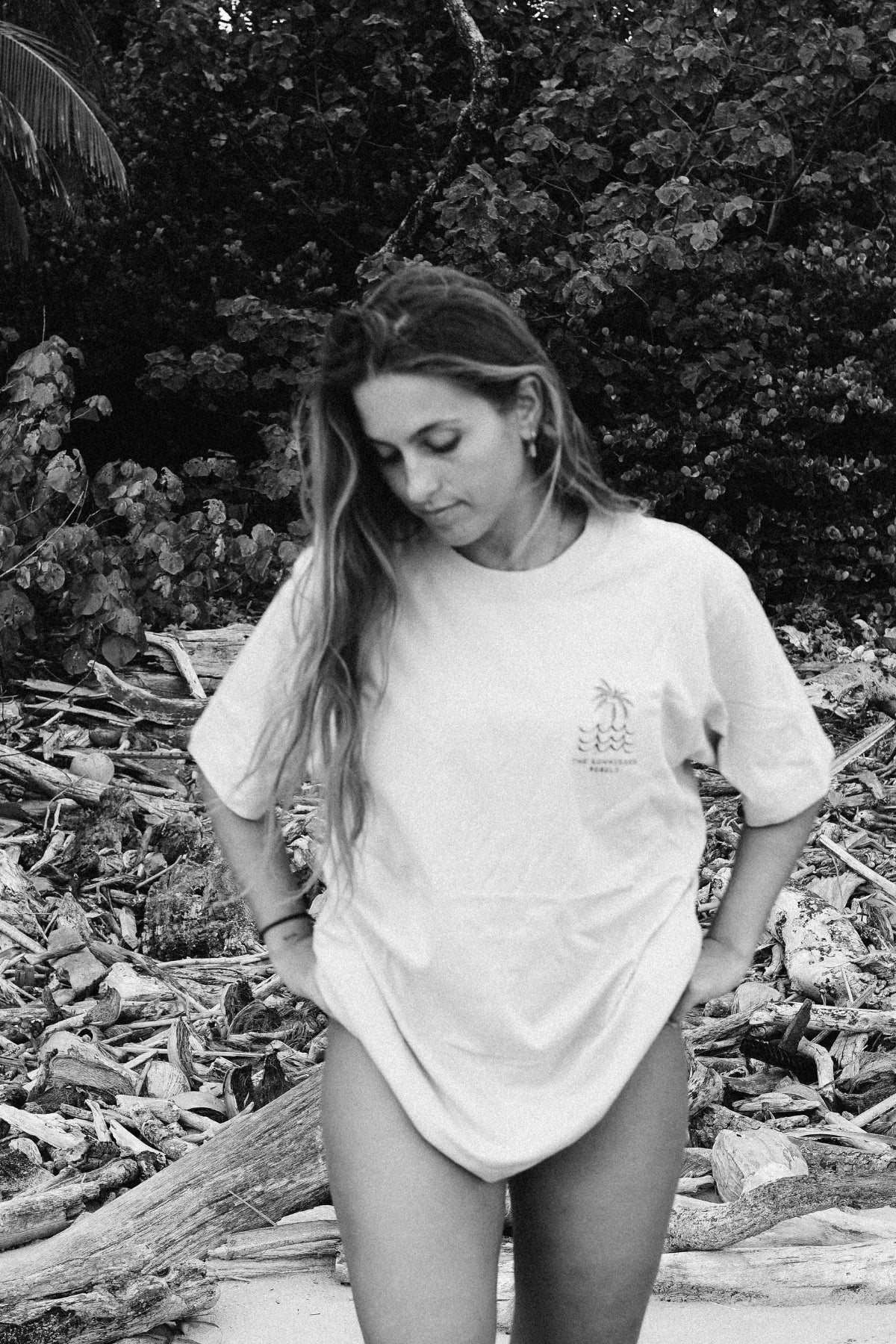 Frau trägt das Waves & Palm Trees Oversized T-Shirt in Sand am Strand in einer stimmungsvollen Schwarz-Weiß-Aufnahme.