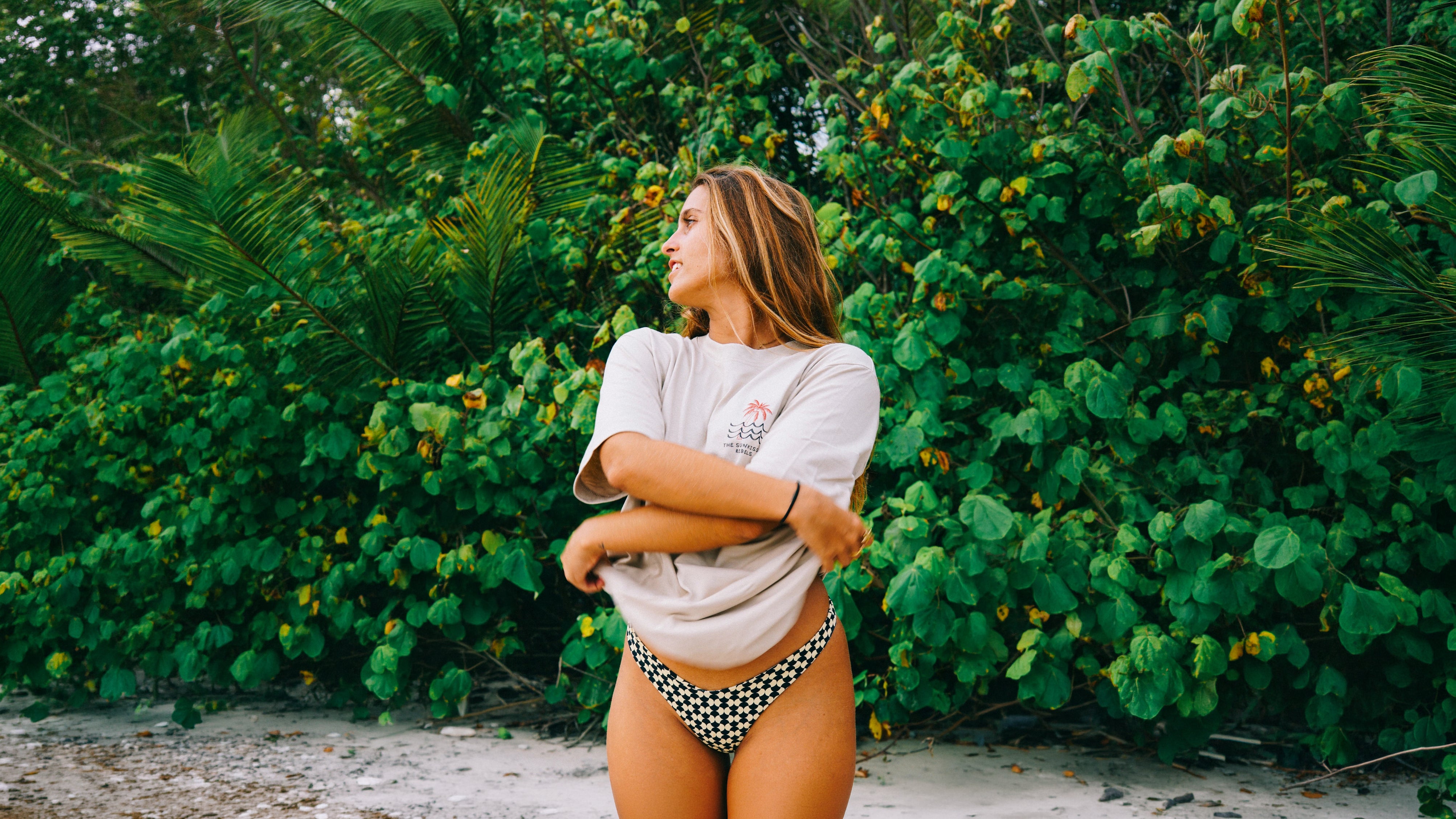 Model von The Sunkissed Rebels Oversized T-Shirts am tropischen Strand und genießt einen entspannten Beach-Lifestyle.