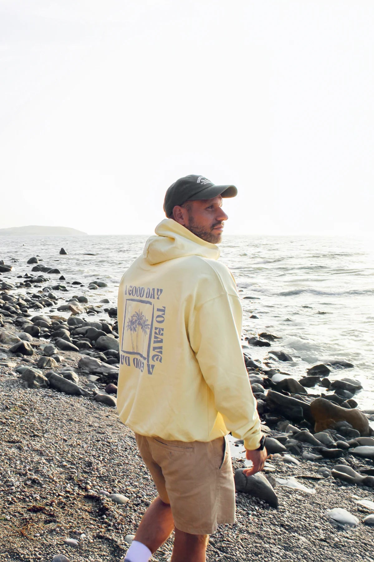 Mann mit A Good Day Oversized Hoodie spaziert am Kiesstrand entlang mit Blick aufs Meer.