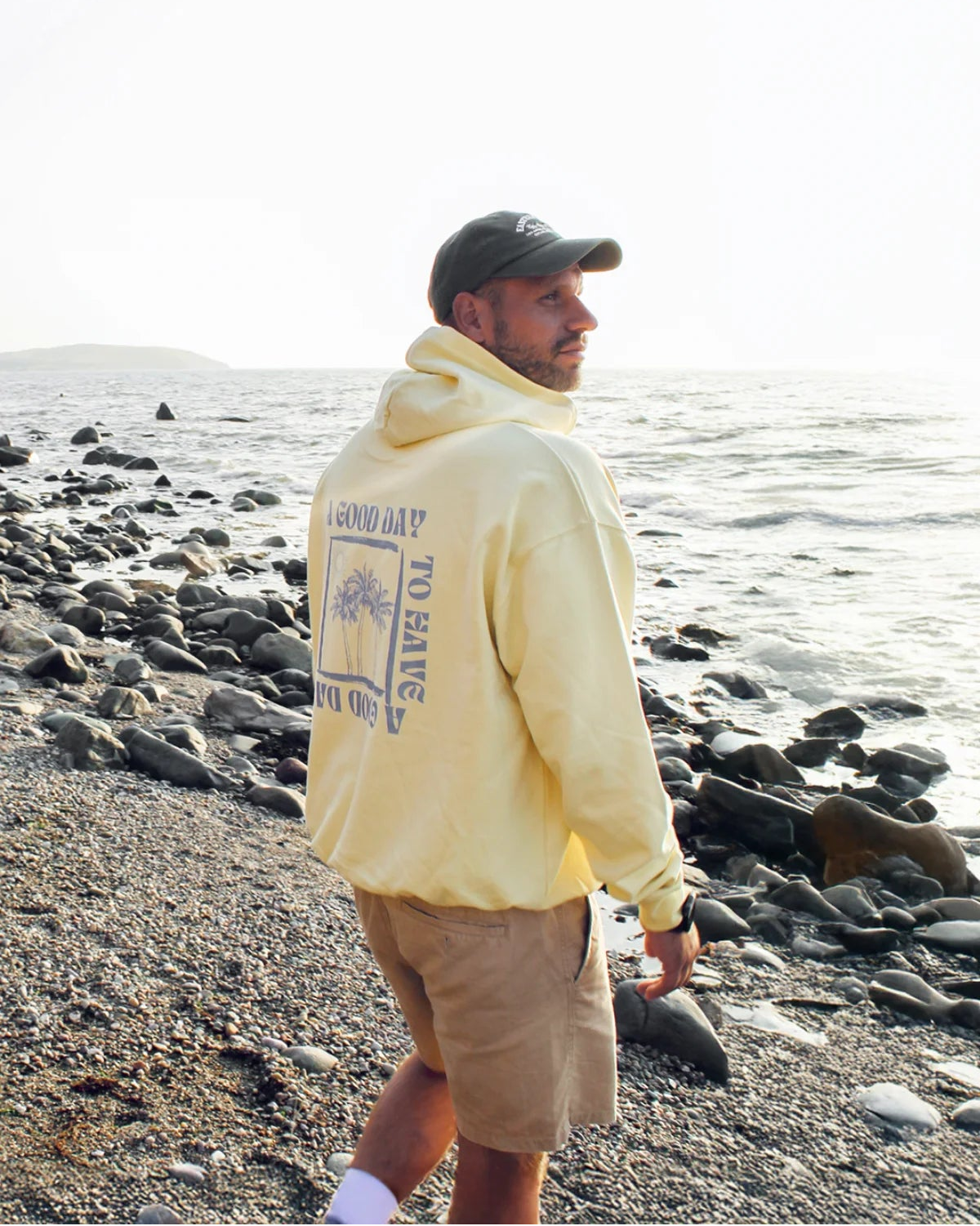 Mann mit A Good Day Oversized Hoodie spaziert am Kiesstrand entlang mit Blick aufs Meer.