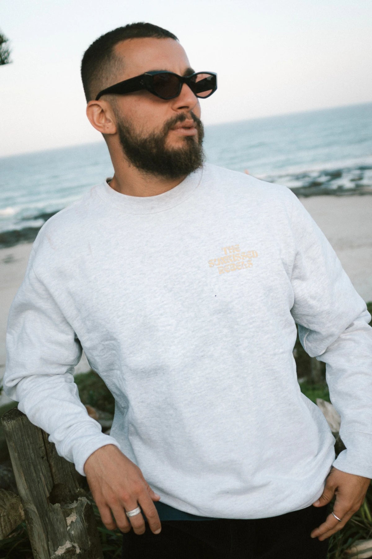 Stilvoller Herrenlook mit dem A Good Day Sweater Cool Grey von The Sunkissed Rebels – Strand und Wellen im Hintergrund.