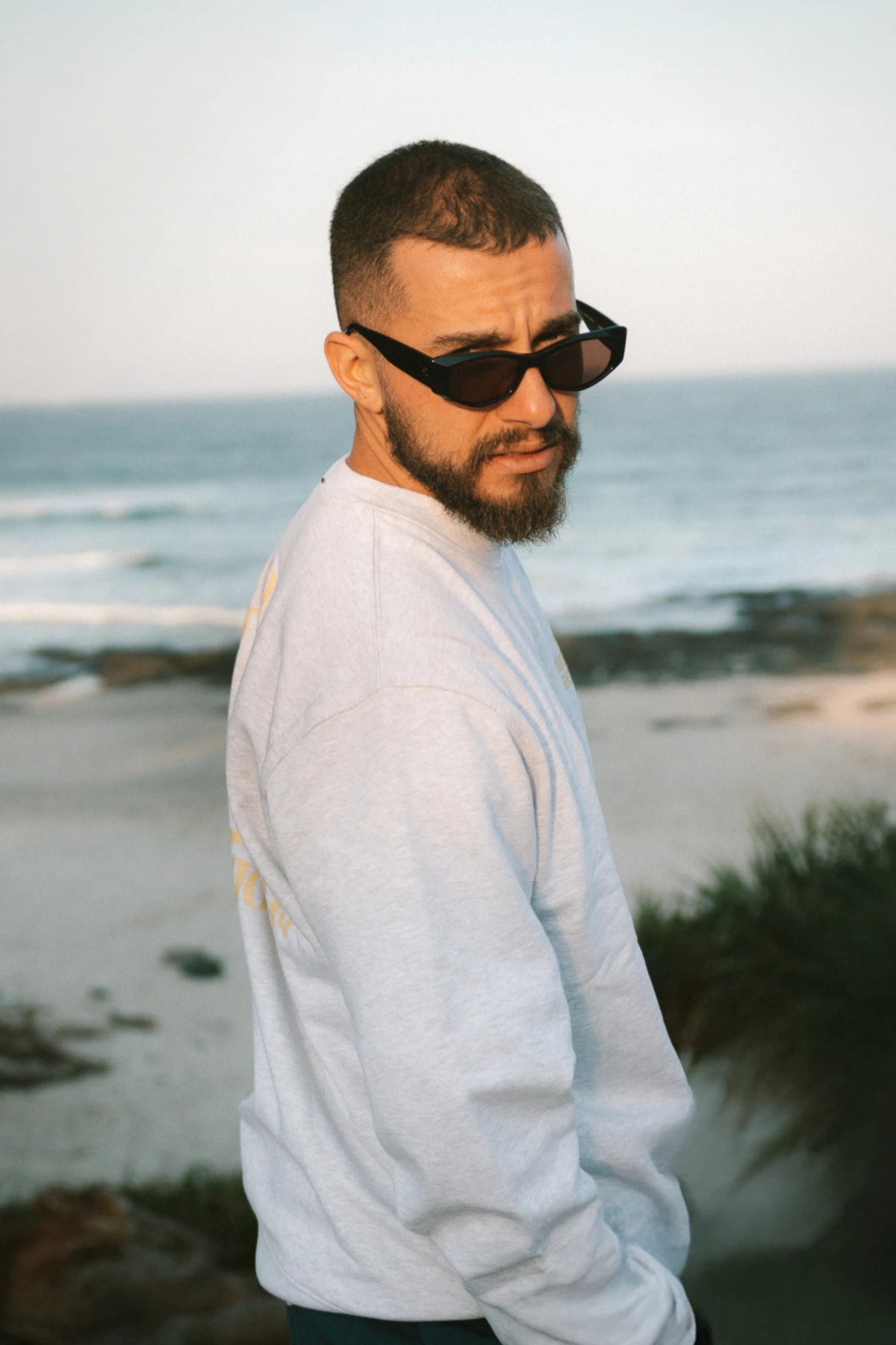 A Good Day Sweater Cool Grey von The Sunkissed Rebels – Rückansicht mit Palmen-Print, fotografiert am Strand.