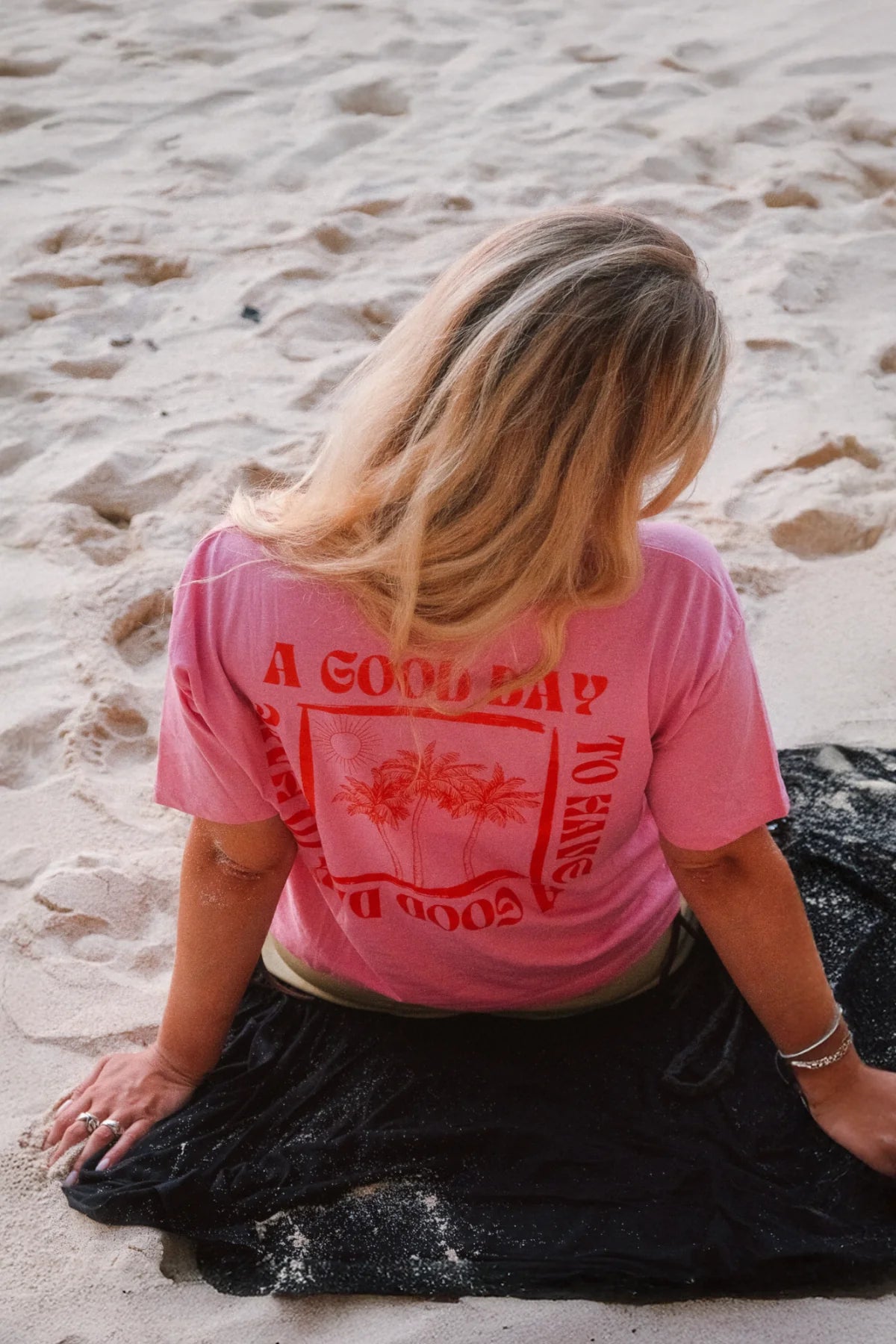 Rückenansicht des A Good Day Women T-Shirts in Pink mit Backprint von The Sunkissed Rebels am Strand