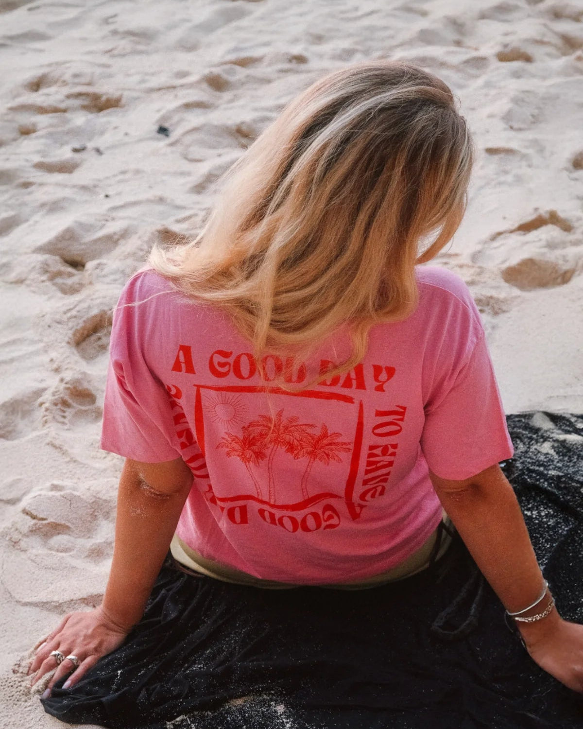 Rückenansicht des A Good Day Women T-Shirts in Pink mit Backprint von The Sunkissed Rebels am Strand
