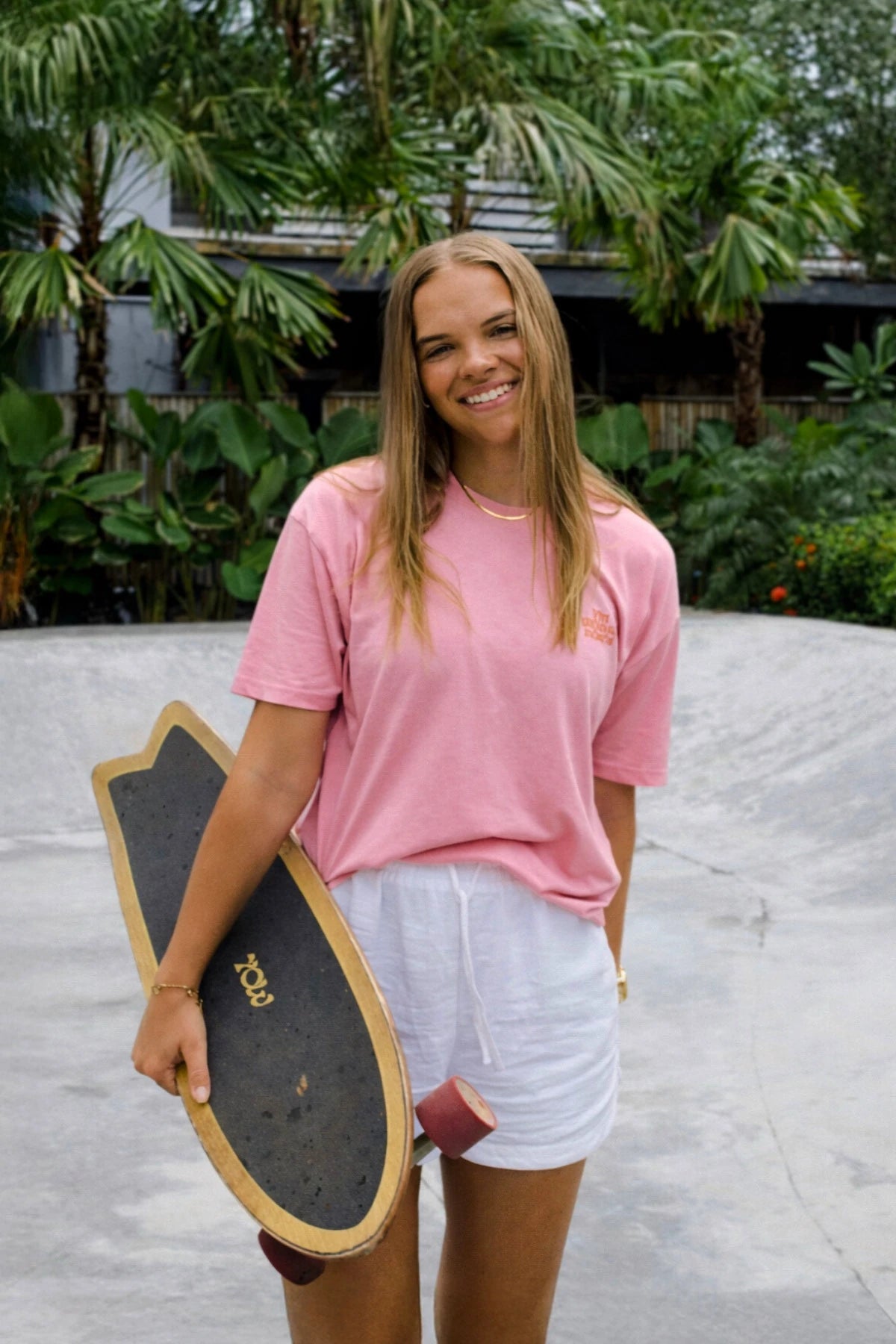 Model von The Sunkissed Rebels trägt das A Good Day Women T-Shirt in Pink beim Skaten im tropischen Lifestyle-Setting