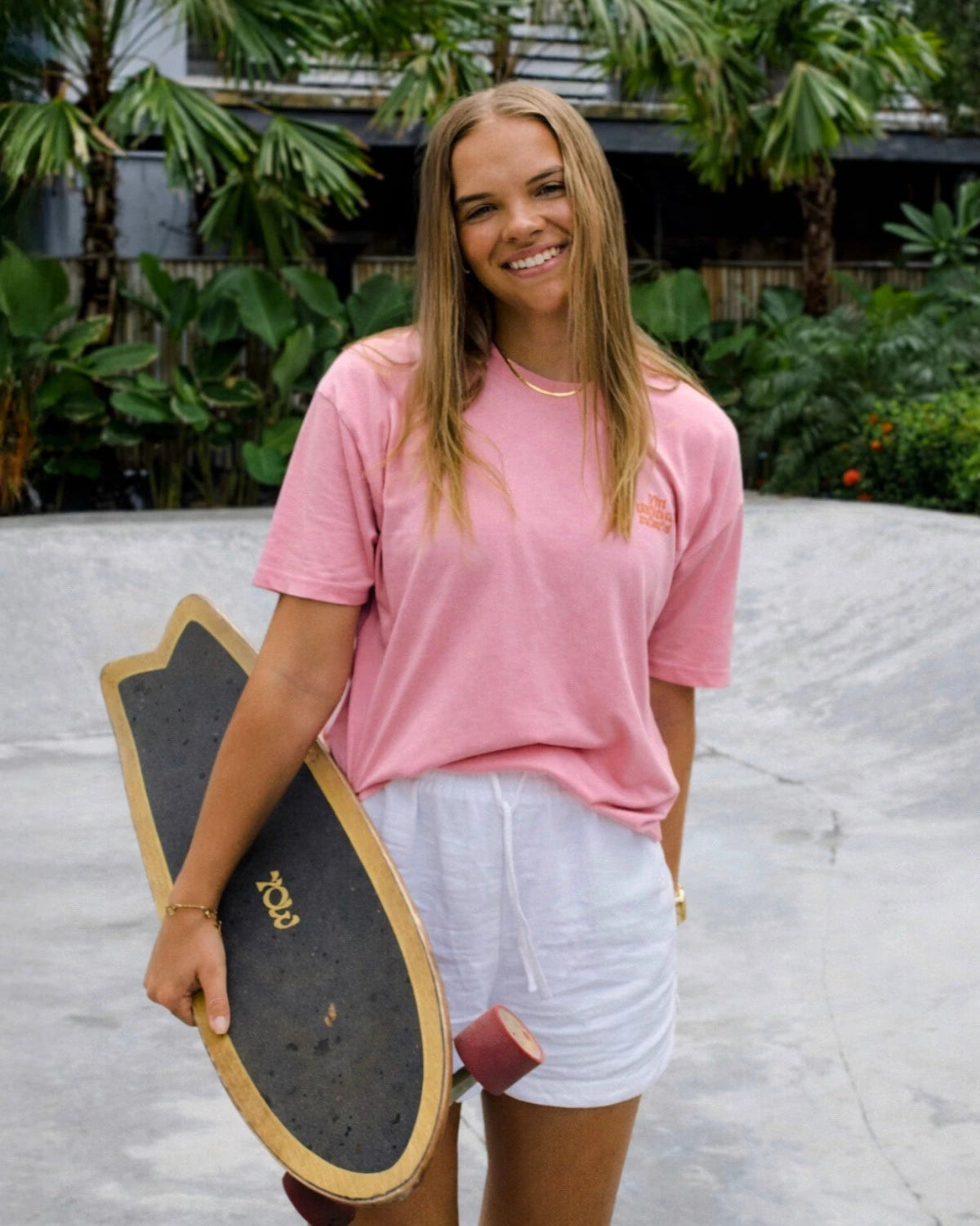 Model von The Sunkissed Rebels trägt das A Good Day Women T-Shirt in Pink beim Skaten im tropischen Lifestyle-Setting