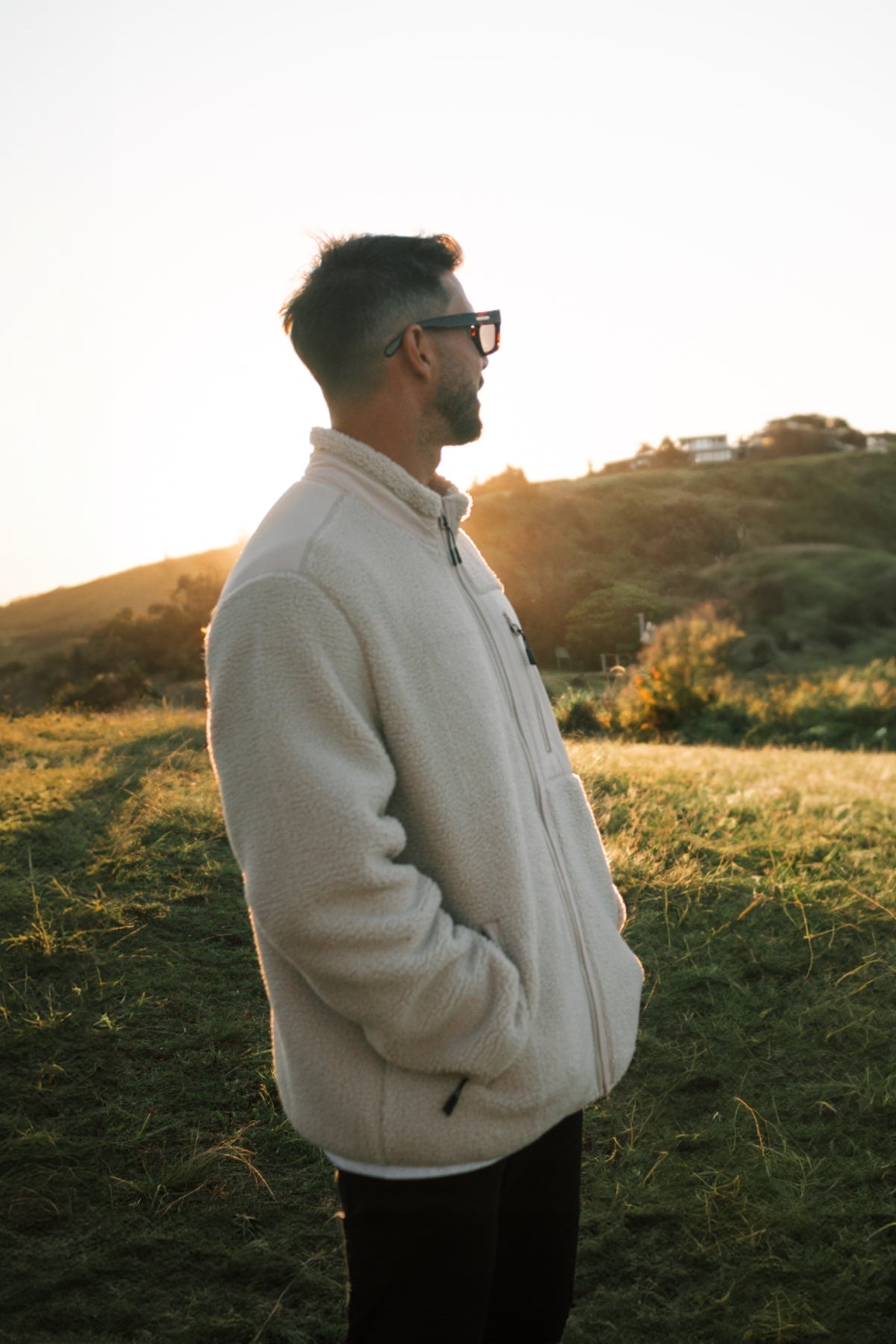 Mann steht auf Hügel in warmer fleece Jacke in beige bei sonnenuntergang