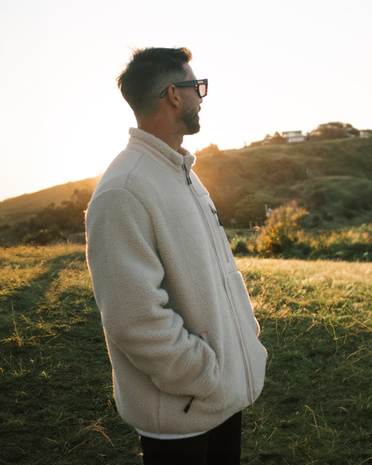 Mann steht auf Hügel in warmer fleece Jacke in beige bei sonnenuntergang