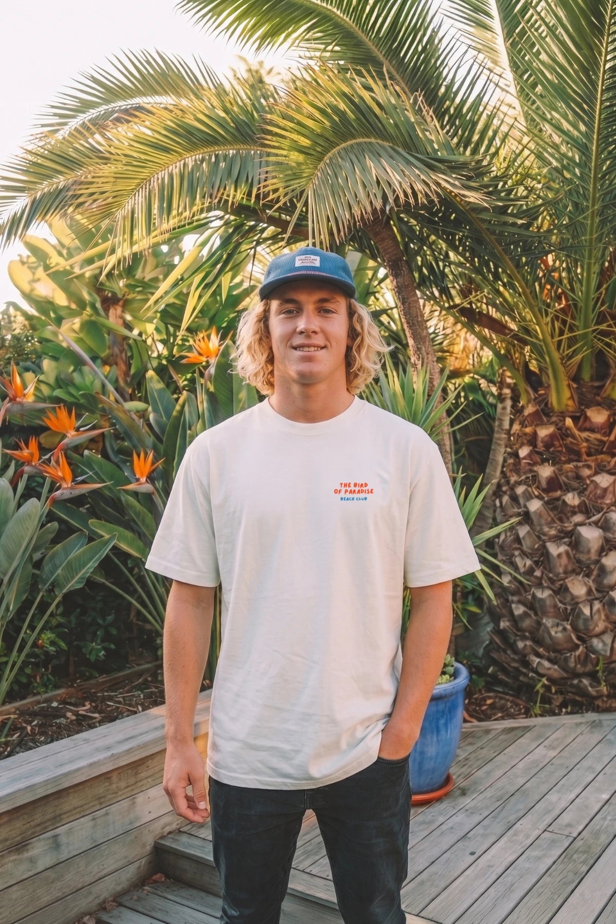 Mann trägt weißes Bird of Paradise Boxy Oversized T-Shirt mit kleinem Frontprint in tropischer Umgebung