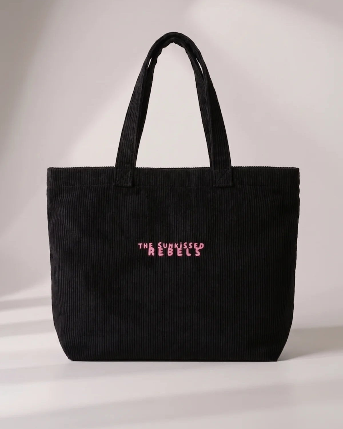 Frontansicht der schwarzen Cord Bag aus Bio-Feincord mit pink gesticktem Schriftzug "The Sunkissed Rebels".